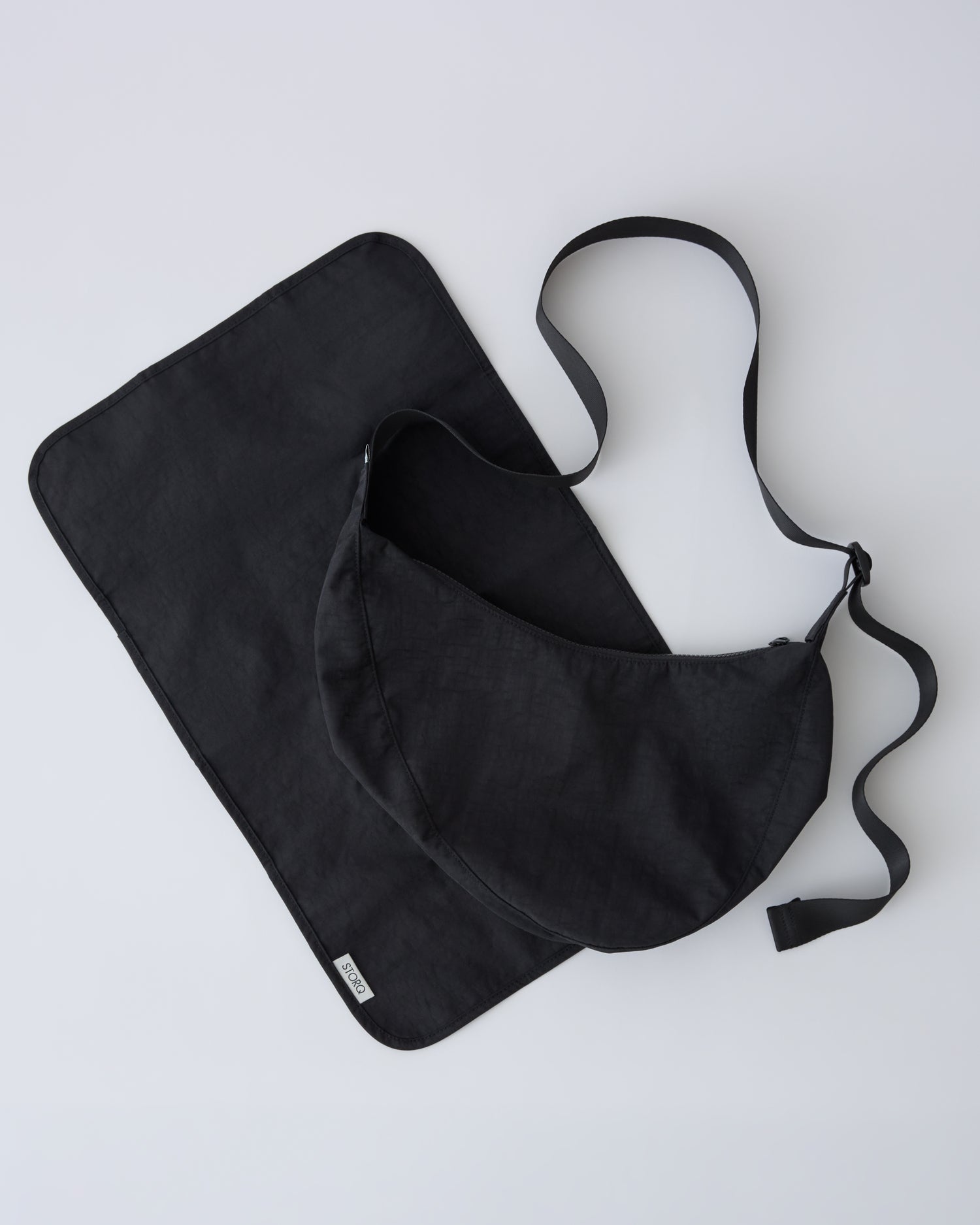Half Moon Crossbody Bag in Black with paired diaper changing mat on a beige background. 