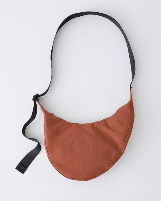 Crescent-shaped Half Moon Bag with Changing Mat in a warm brown Cinnamon, featuring a black adjustable strap, laid flat against a light gray background.