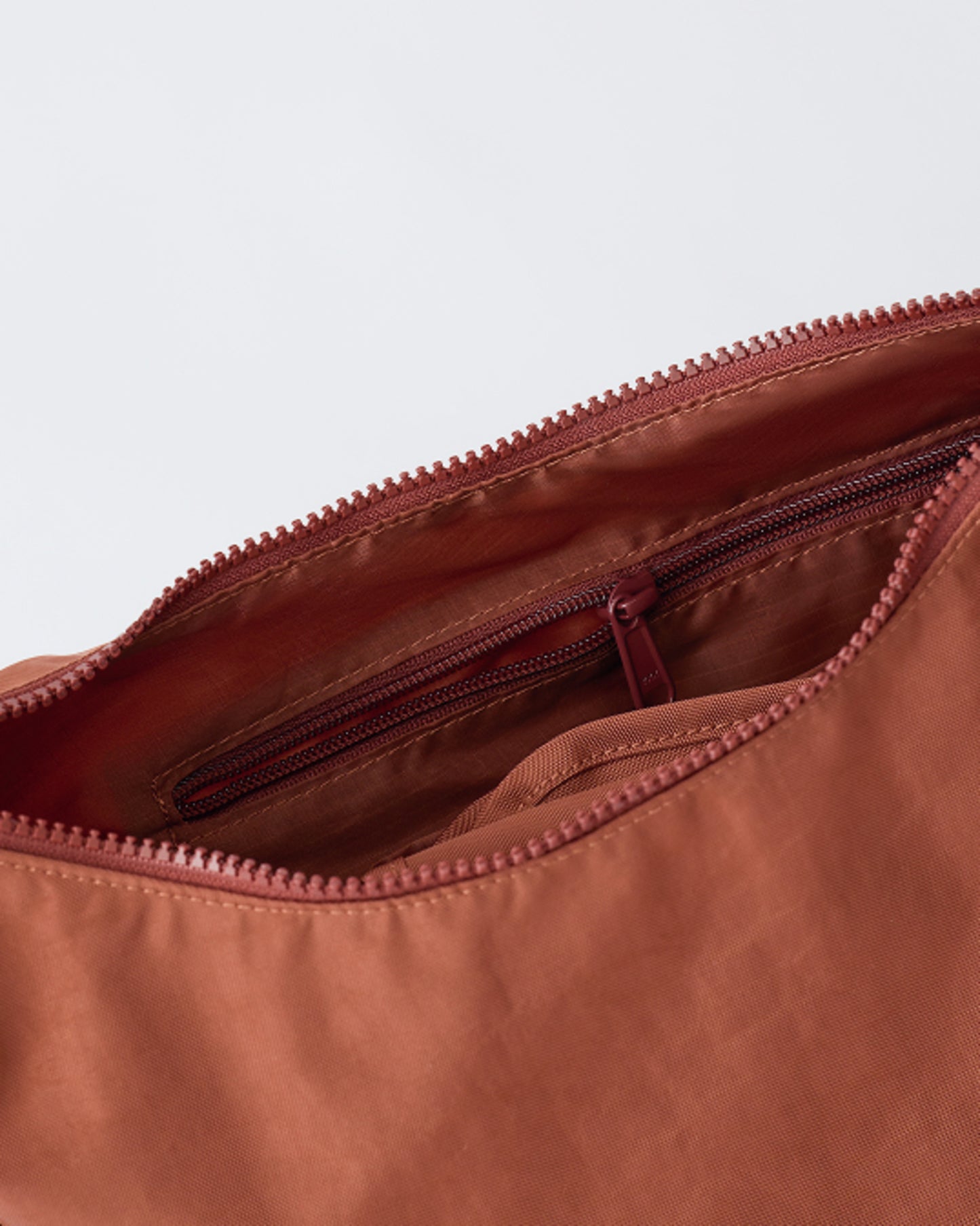 Close up of the zipper and pocket of Half Moon Crossbody Bag in Cinnamon, a beige background.