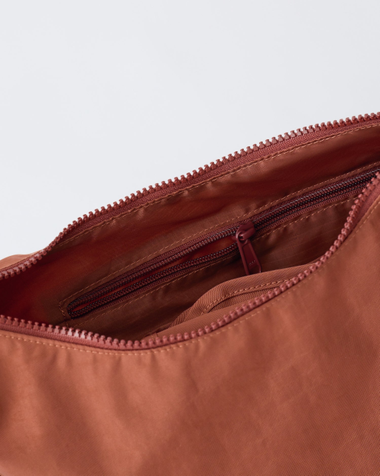 Close up of the zipper and pocket of Half Moon Crossbody Bag in Cinnamon, a beige background.
