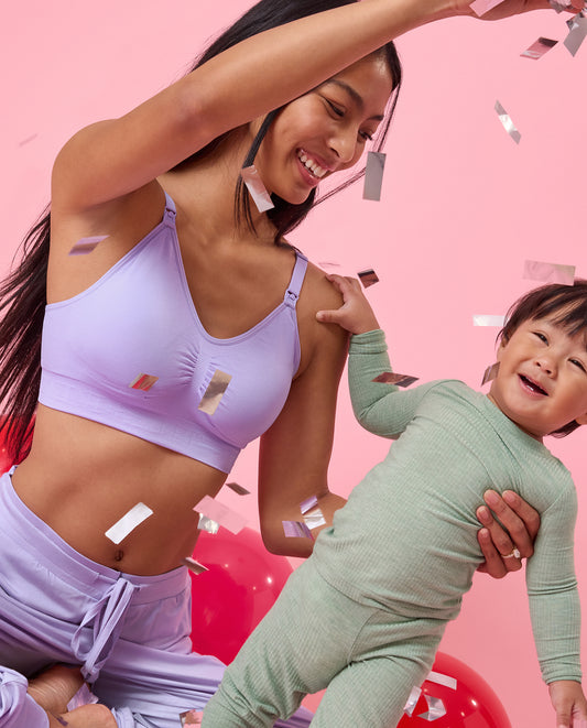 Woman in a purple bra and pants holding a child against a pink background