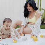 Model sitting on blanket on grass with baby wearing the Sublime® Hands-Free Pumping & Nursing Bra in Light Lemon, paired with the Reese Oversized Linen Button Down Shirt and the Reese Linen Short in Natural