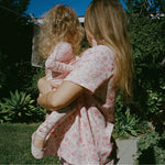 Mother and daughter wearing matching pajamas in their sunny, lush yard. Woman is wearing Cotton Bamboo Pajama Set in Pink Toile and daughter is wearing Bamboo Baby Pajama in Pink Toile and soft ballet shoes.