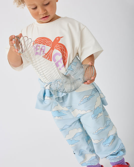 A toddler wearing Graphic Tee in White Bird, paired with French Terry Jogger in Blue Clouds, holding a clear plastic slinky against a plain light gray background.