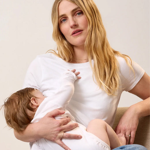 Model wearing Classic Cotton Nursing T-shirt in White on a beige background nursing a baby in a white long sleeve onesie.