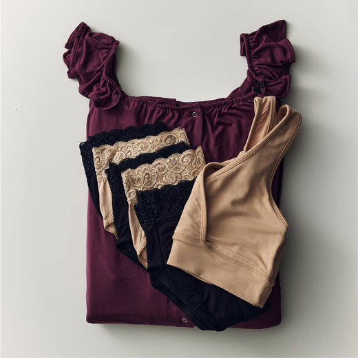 Flat lay of Labor & Delivery Essentials Bundle including a Ruffle Labor & Delivery Gown, High-Waisted Postpartum Recovery Underwear (five-pack) and a French Terry Racerback Nursing Bra on a beige background