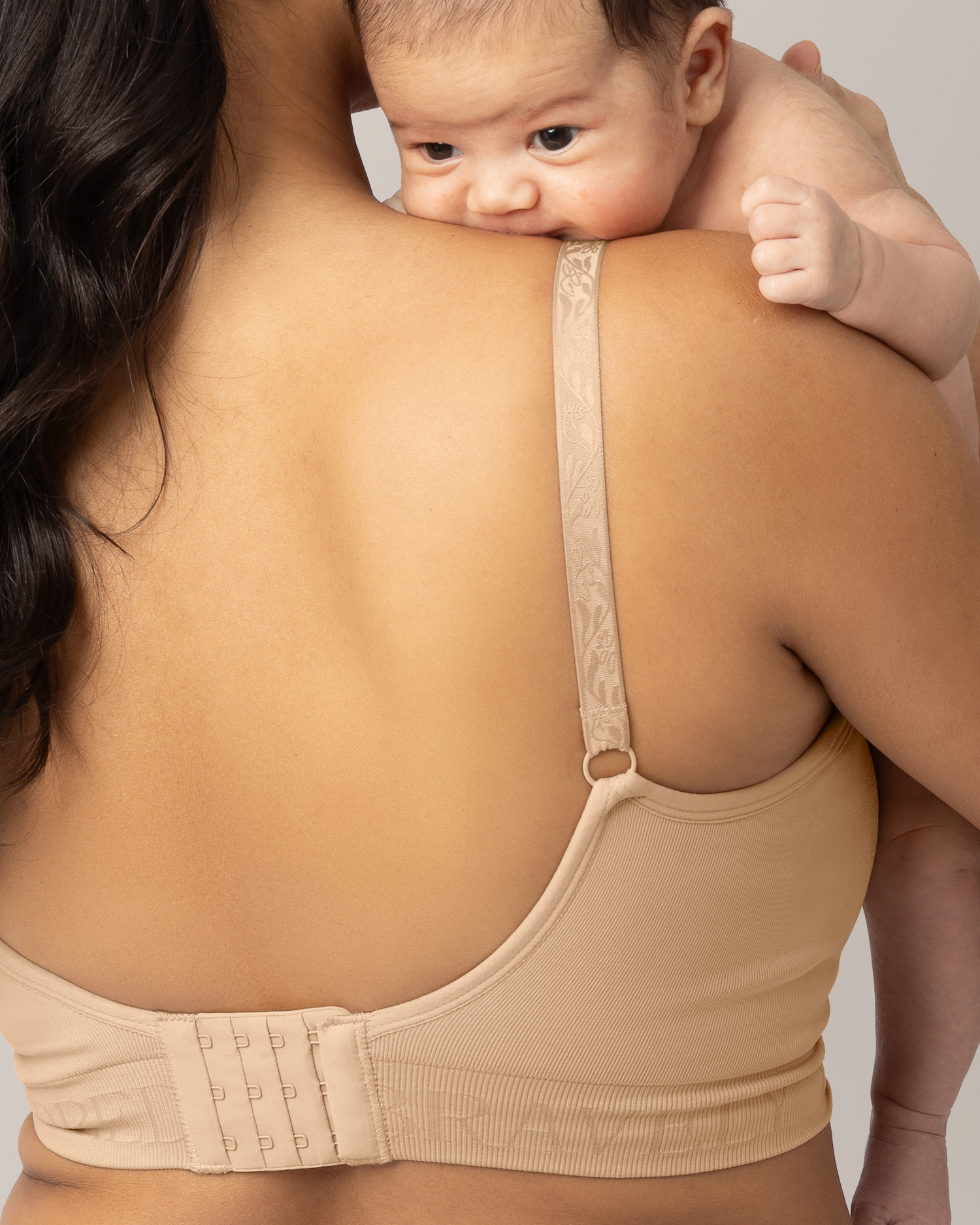 Woman wearing a beige bra holding a baby against a neutral background