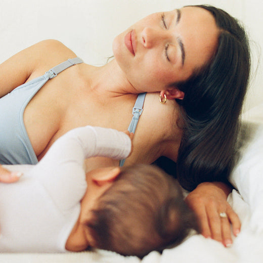 Mother resting on her side while breastfeeding baby and wearing French Terry Maternity & Nursing Bralette in Vintage Blue on a white background.