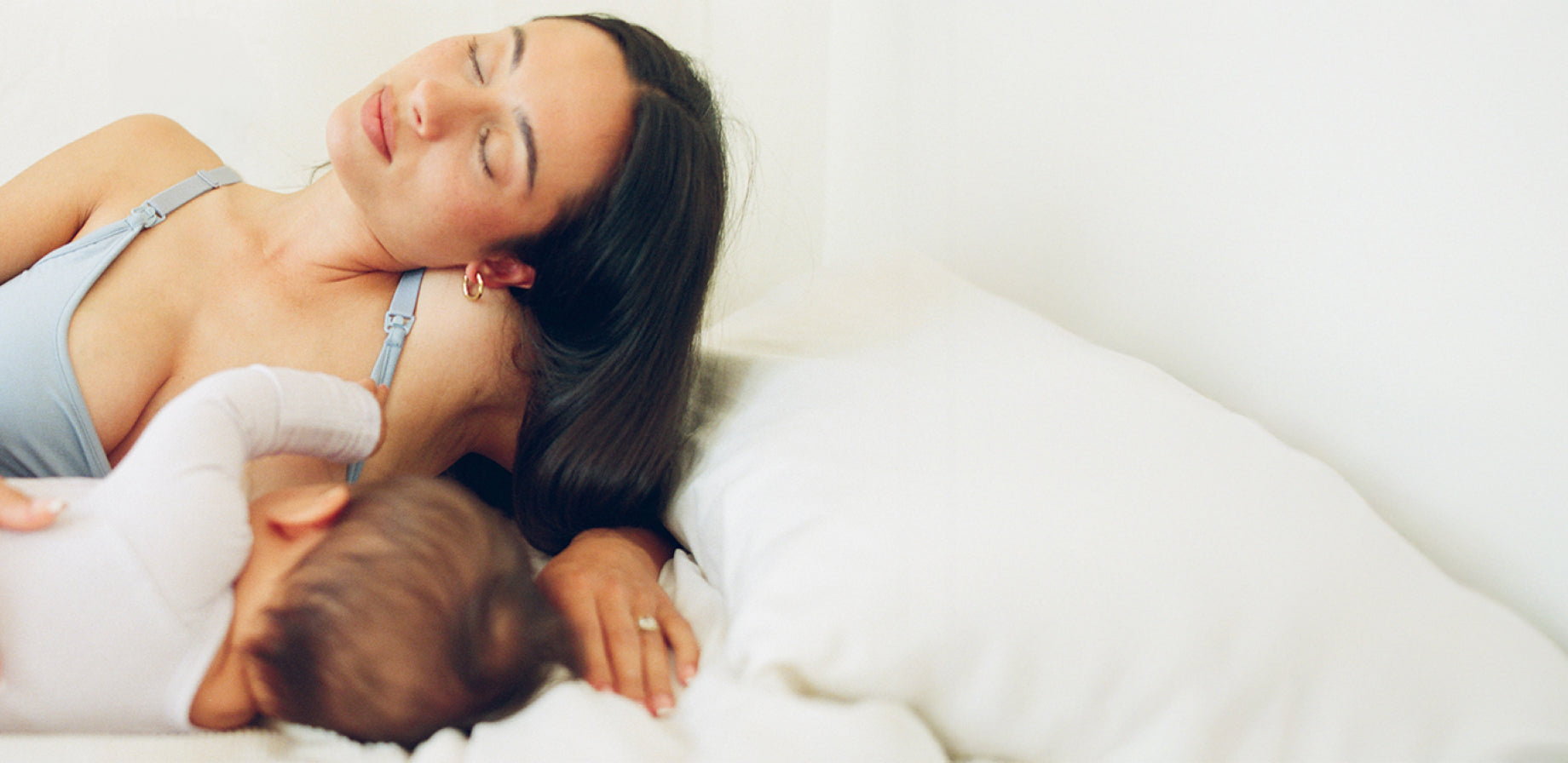 Mother resting on her side while breastfeeding baby and wearing French Terry Maternity & Nursing Bralette in Vintage Blue on a white background.