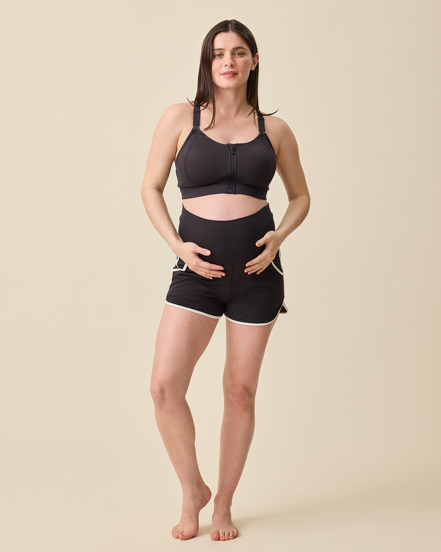 Model is displaying the foldable waistband on the Active Maternity & Postpartum Short - and High Impact Nursing Sports Bra in Black on a beige background