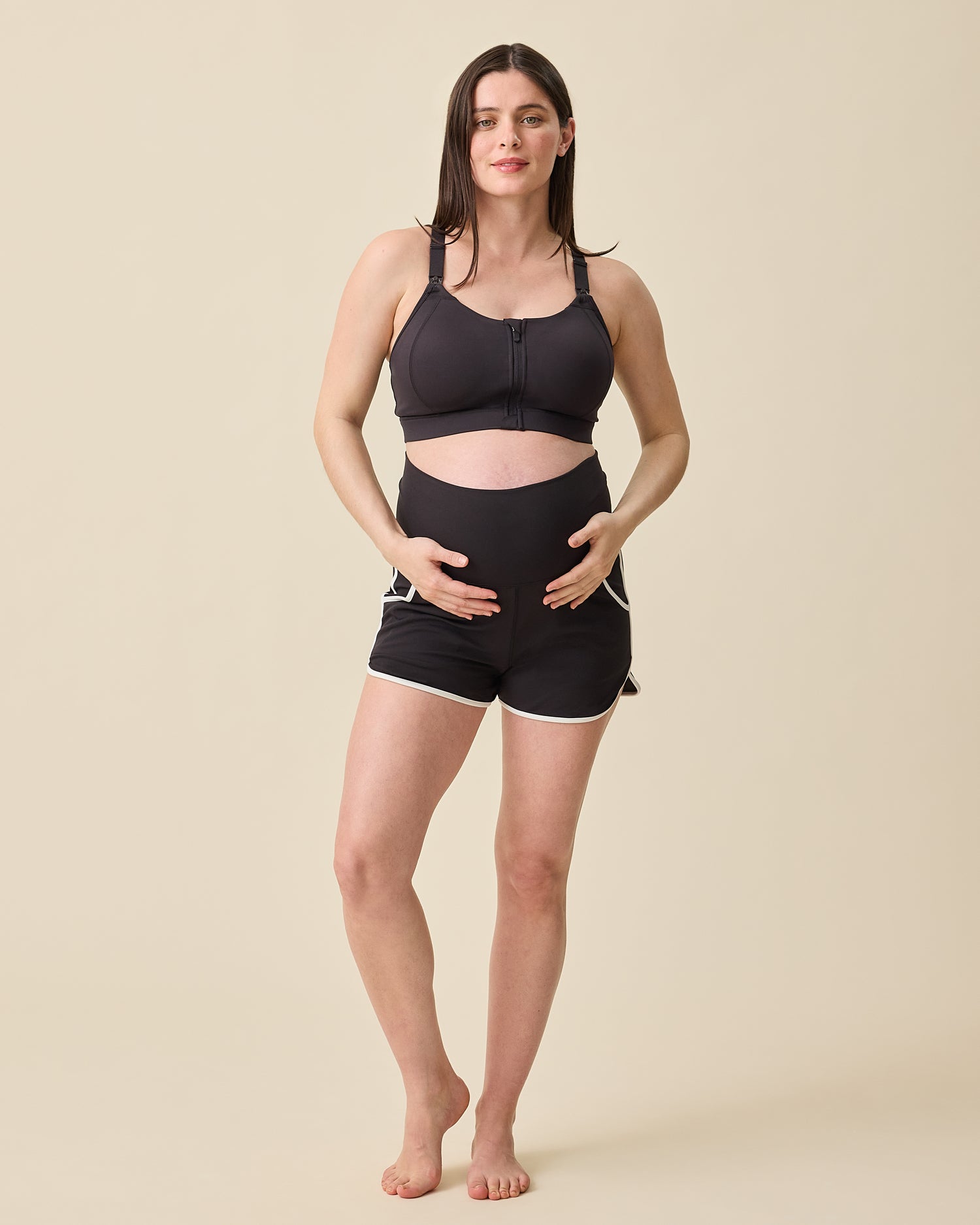 Model is displaying the foldable waistband on the Active Maternity & Postpartum Short - and High Impact Nursing Sports Bra in Black on a beige background