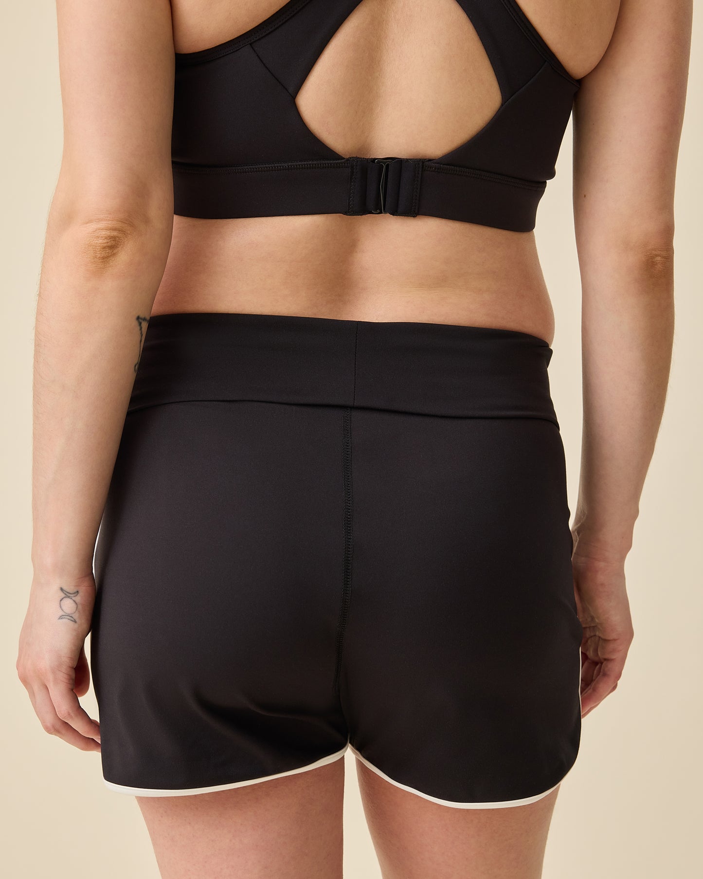 Back view of model wearing Active Maternity & Postpartum Short - and High Impact Nursing Sports Bra in Black on a beige background