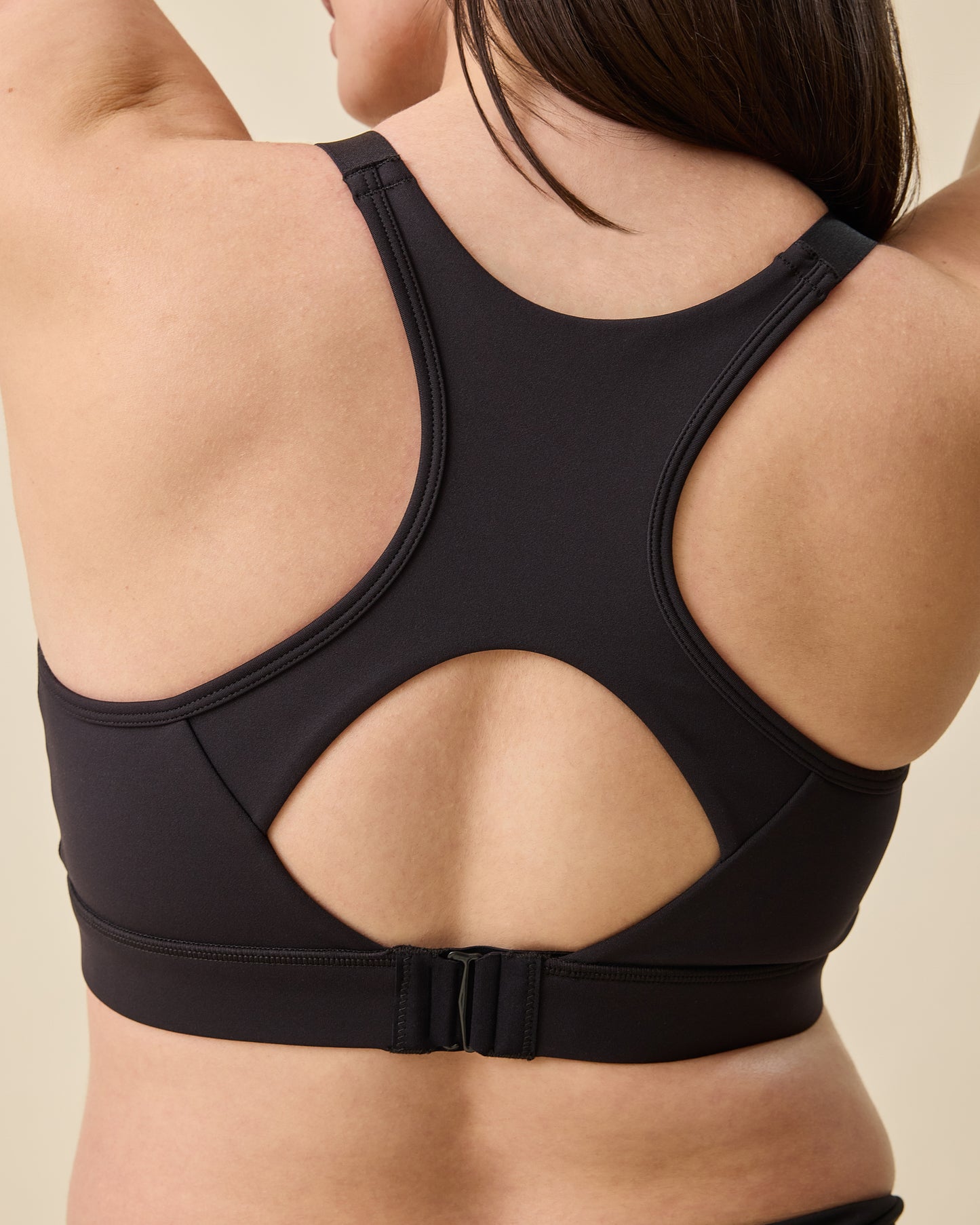 Back view on the High Impact Nursing Sports Bra in Black on a beige background