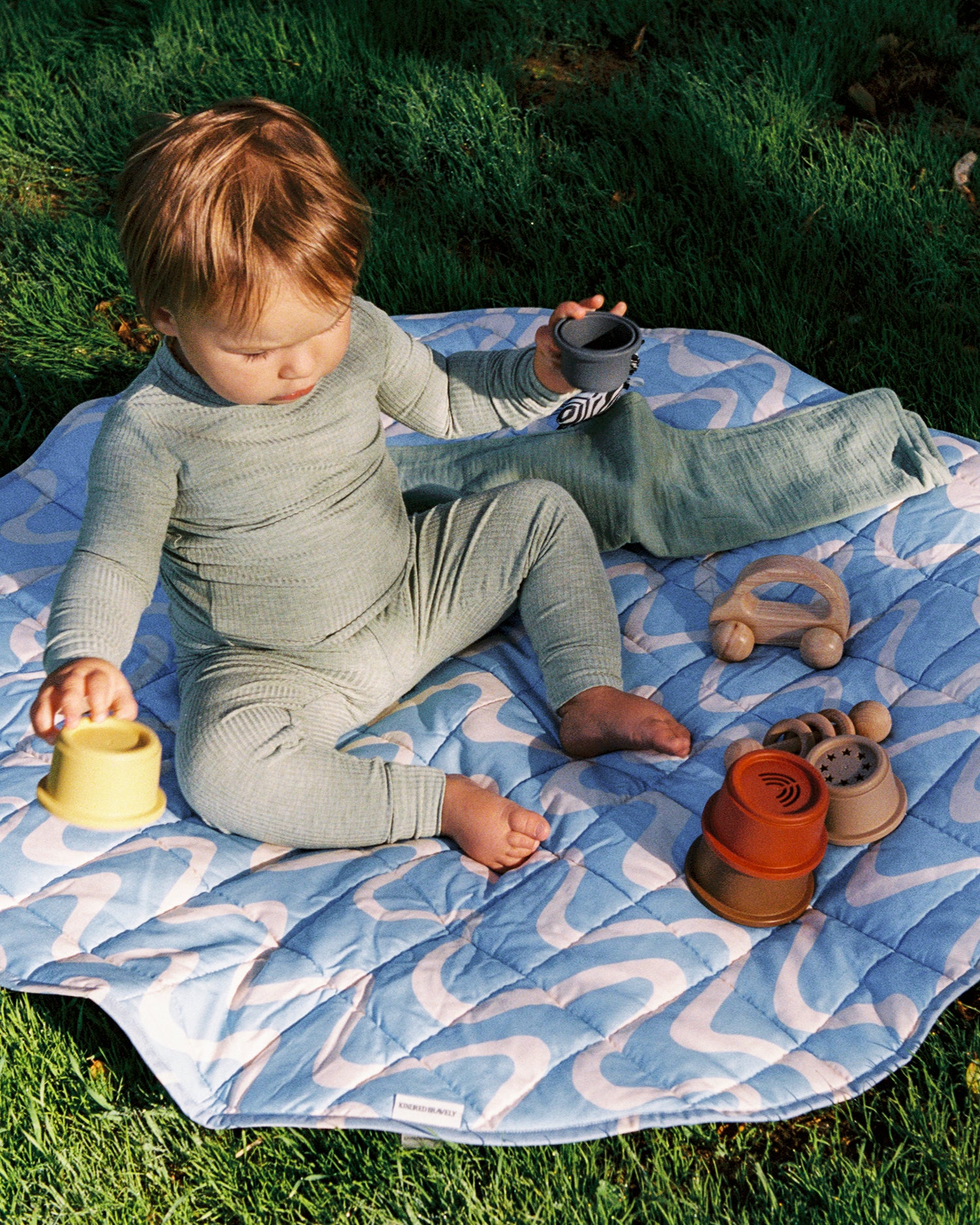 Child playing with toys on the The Inside/Outside Play Mat in Blue Waves print outdoors