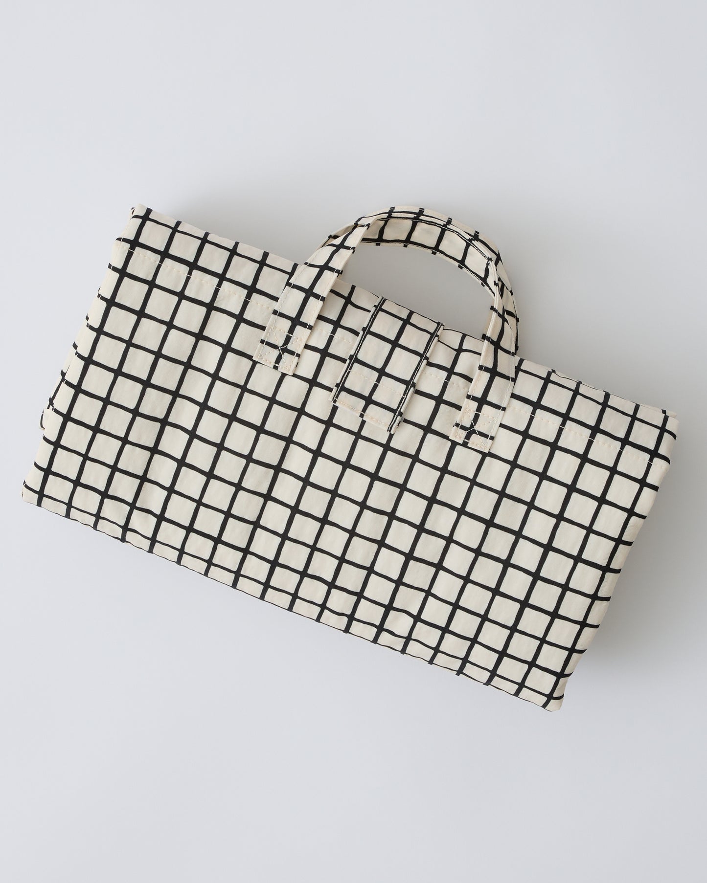 Inside/Outside Play Mat in Black Grid folded up and ready to go, on a beige background.