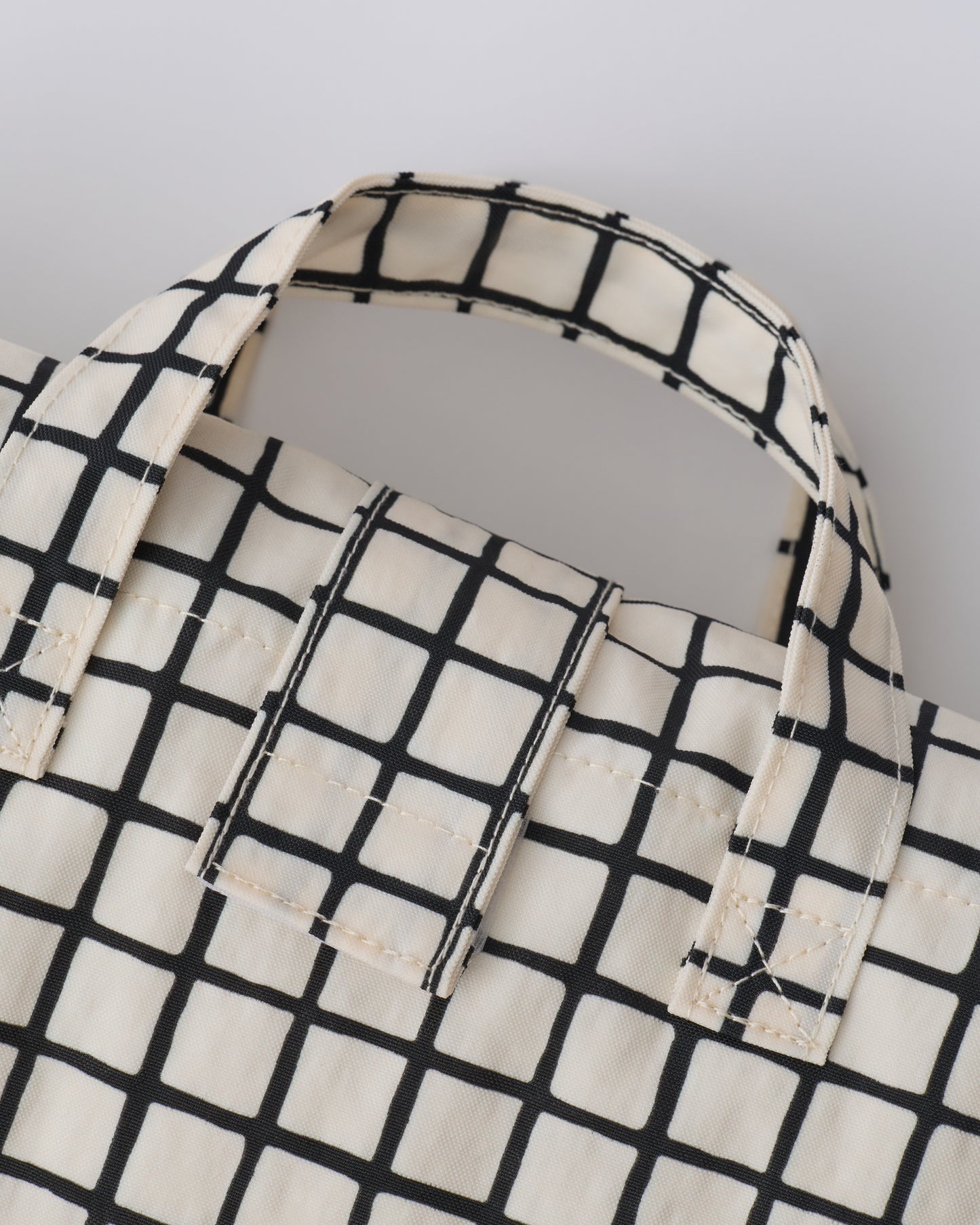 Close up of handle of the folded up Inside/Outside Play Mat in Black Grid on a beige background.