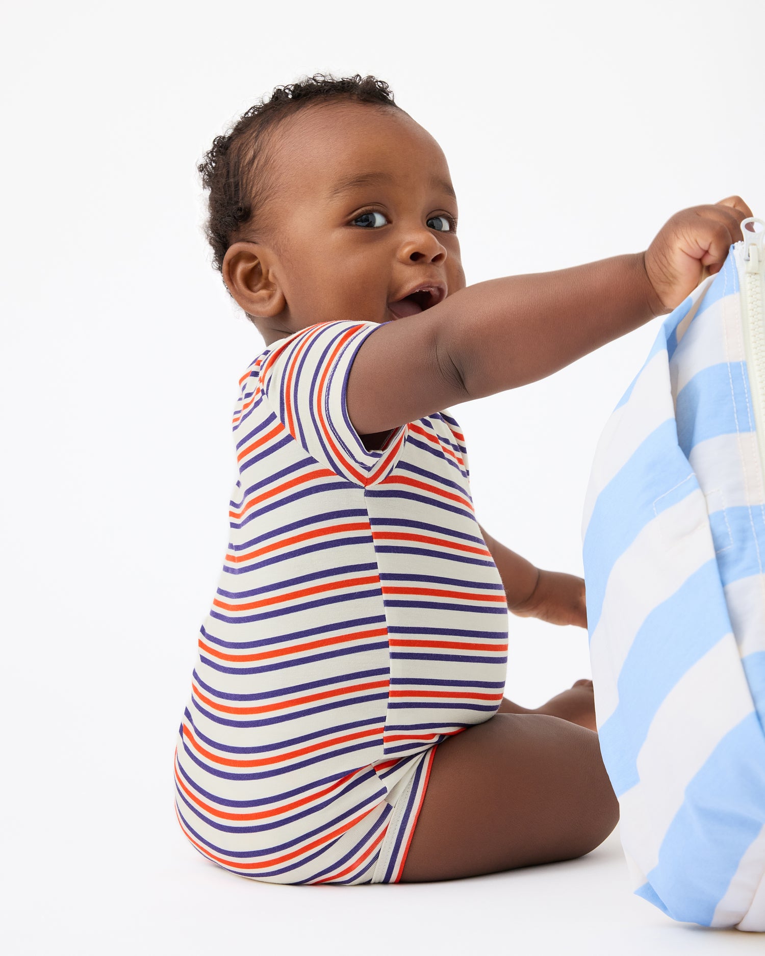 Baby is playing with bag and wearing Baby Onesie Two-Pack in Red & Blue Stripe on a beige background