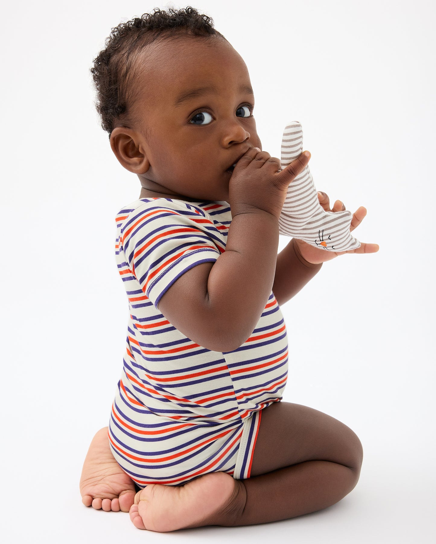 Baby is playing with toy and wearing Baby Onesie Two-Pack in Red & Blue Stripe on a beige background@model_info:Jobadaiah is wearing 6-12 months.