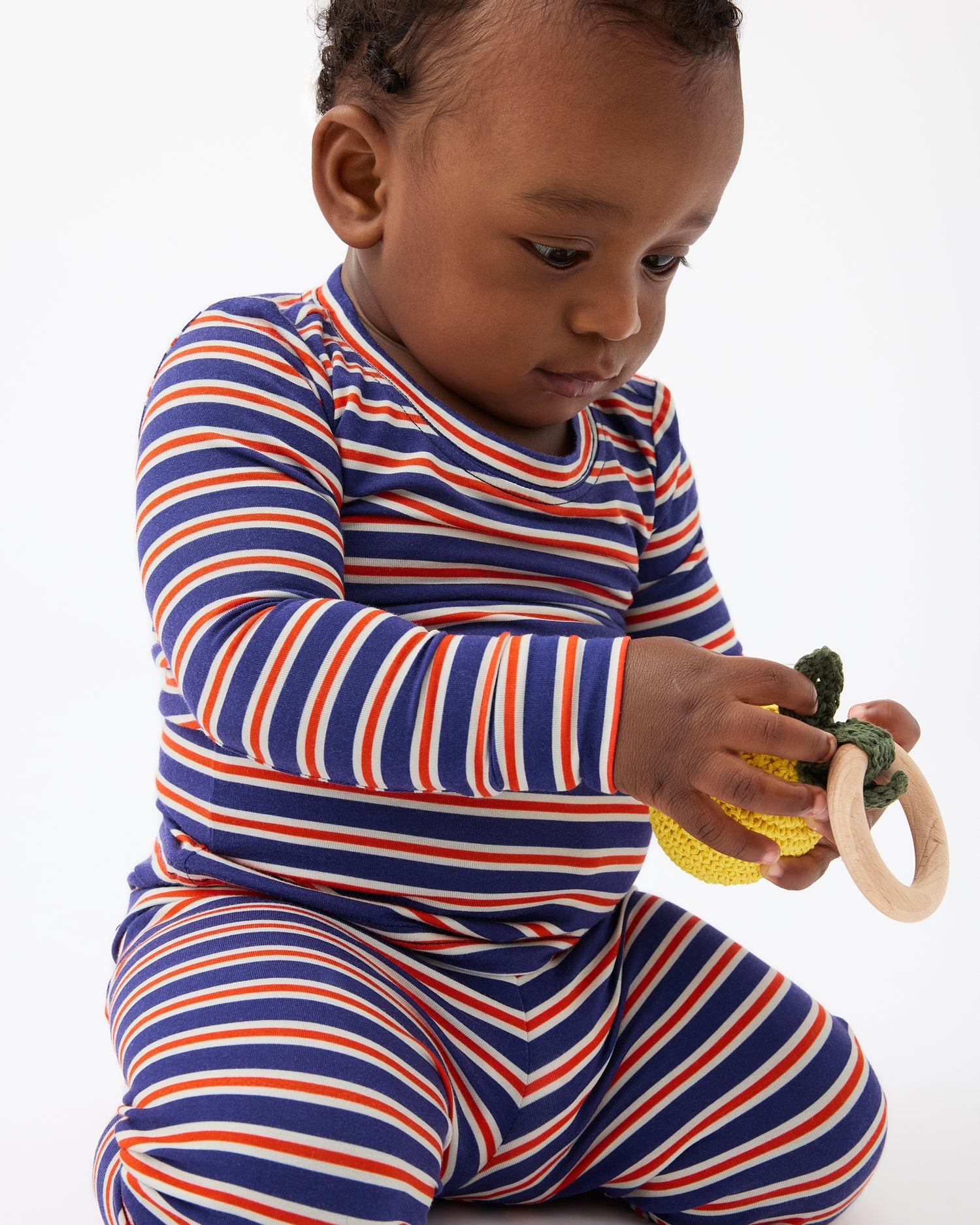 Baby is playing with chew toy and wearing Bamboo Baby Two-Piece Pajama Set in Preppy Stripe on a beige background