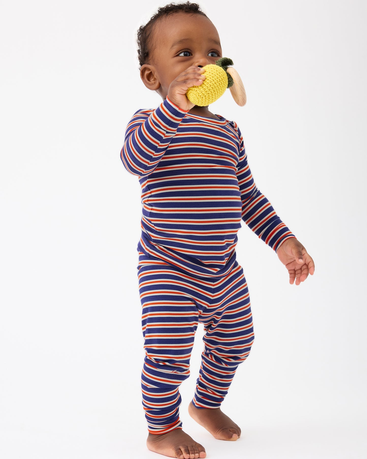 Baby is playing with a chewy toy and wearing Bamboo Baby Two-Piece Pajama Set in Preppy Stripe on a beige background