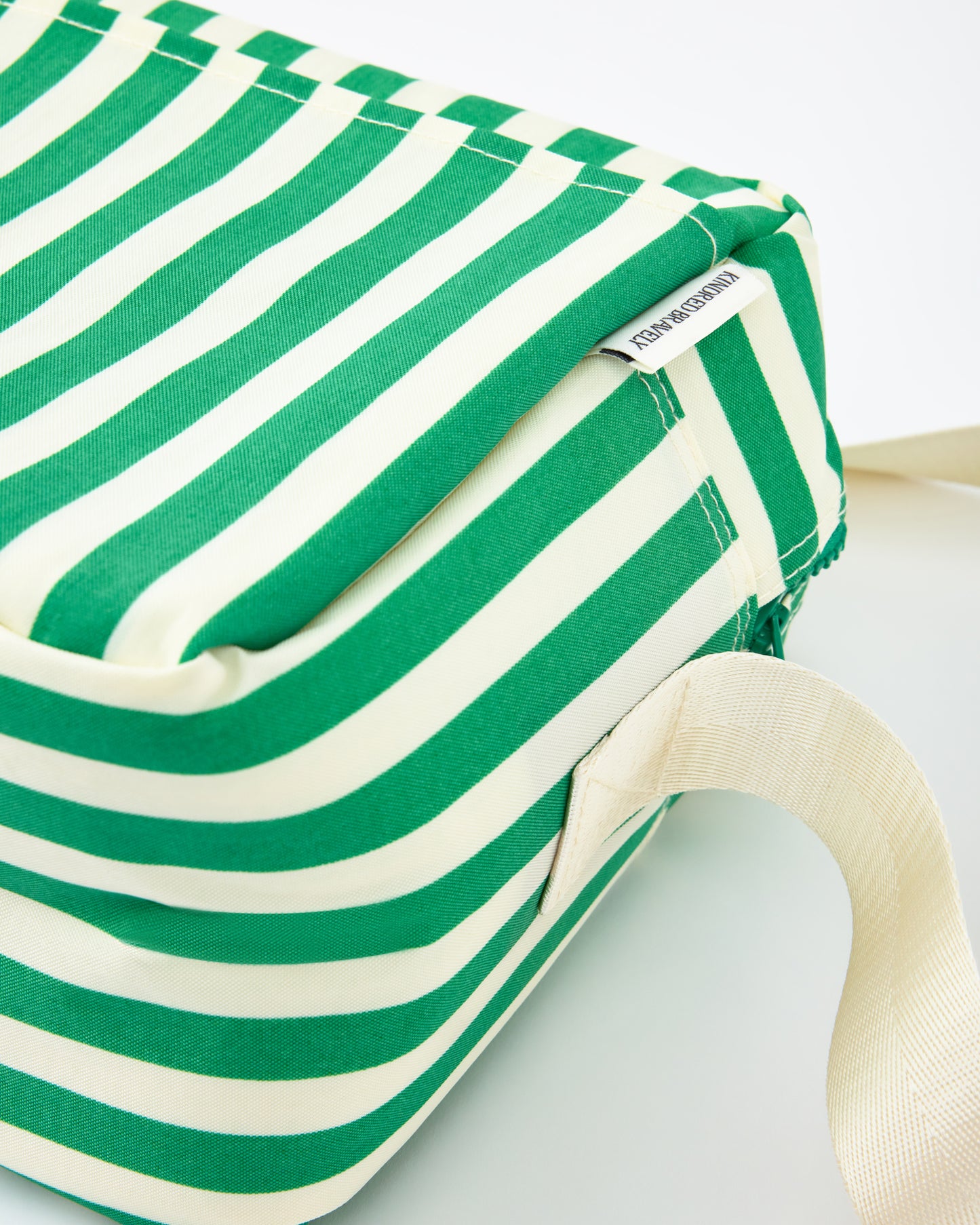Close up of side and strap of the Jumbo Cooler Bag in Green Stripe, on a beige background.