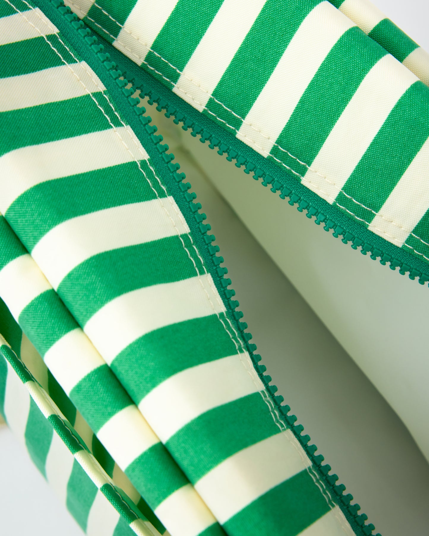 Close up of open zipper of the Jumbo Cooler Bag in Green Stripe, on a beige background.