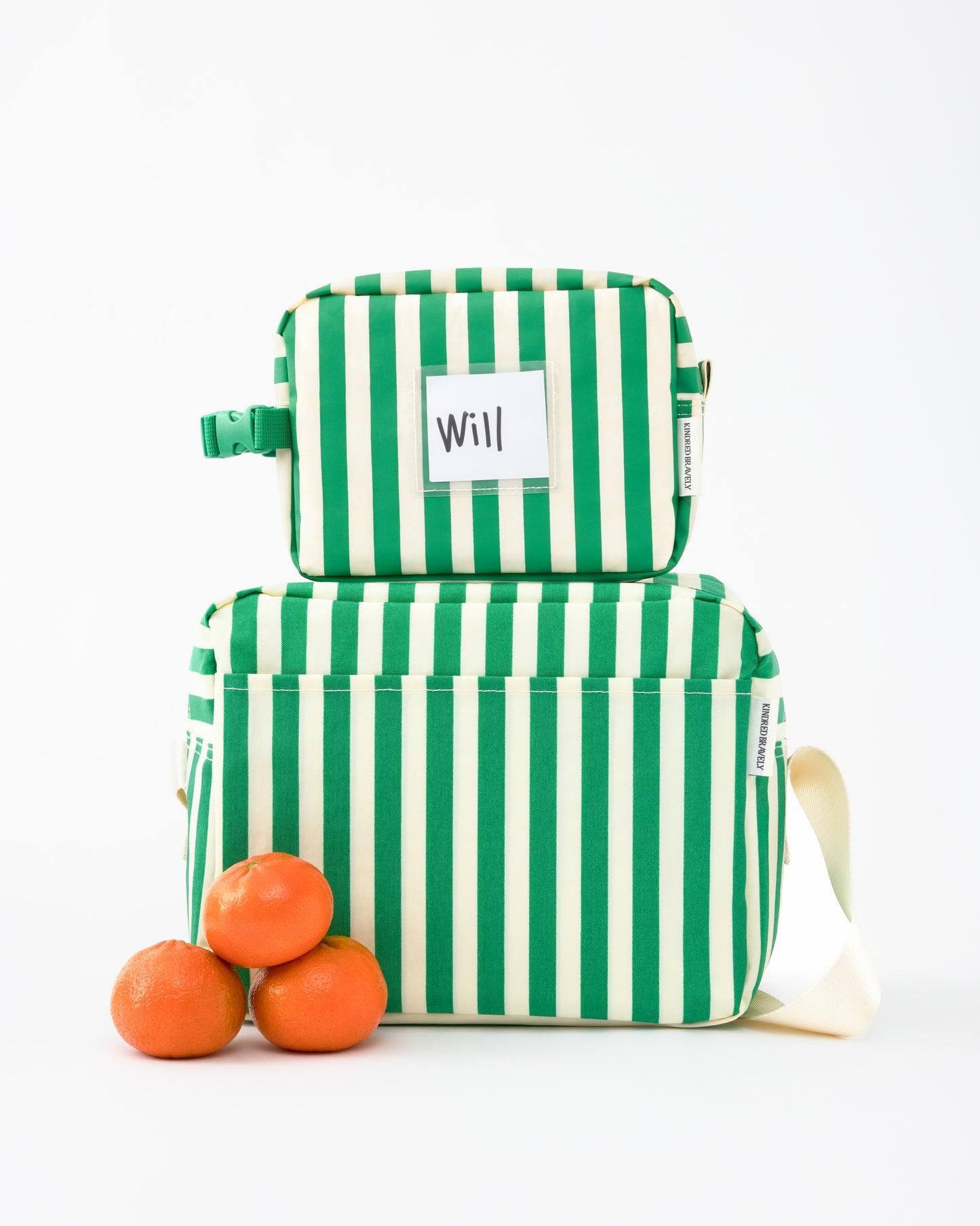 Mini Cooler Bag in Green Stripe stacked ontop of the Jumbo Cooler Bag in Green Stripe, next to three stacked oranges, on a beige background.