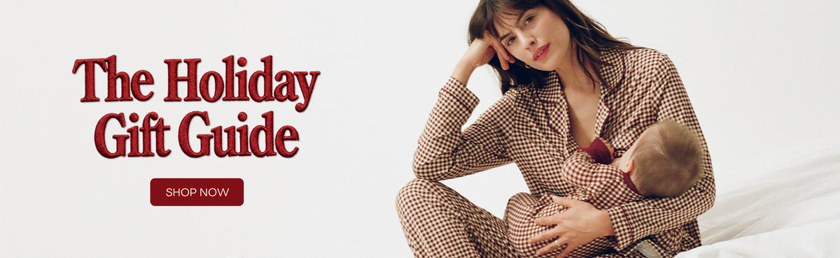 A woman in Clea Bamboo Long Sleeve Pajama Set in Auburn Gingham sits on a white bed holding a baby, with large red text reading 'The Holiday Gift Guide' and a 'SHOP NOW' button on the right.