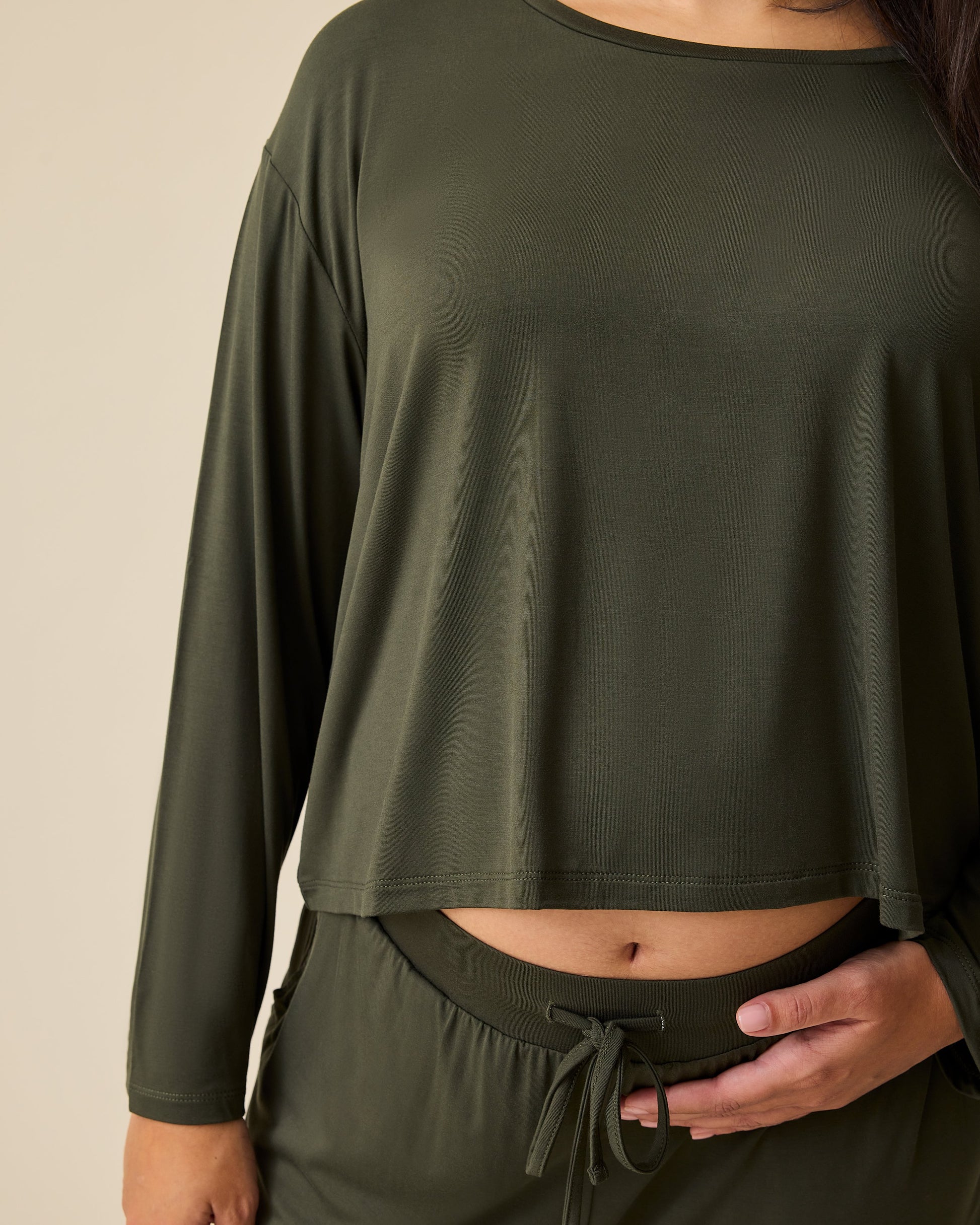 Close up of the sleeve on model wearing Aria Bamboo Casual Cropped Long Sleeve Top in Thyme on a beige background.