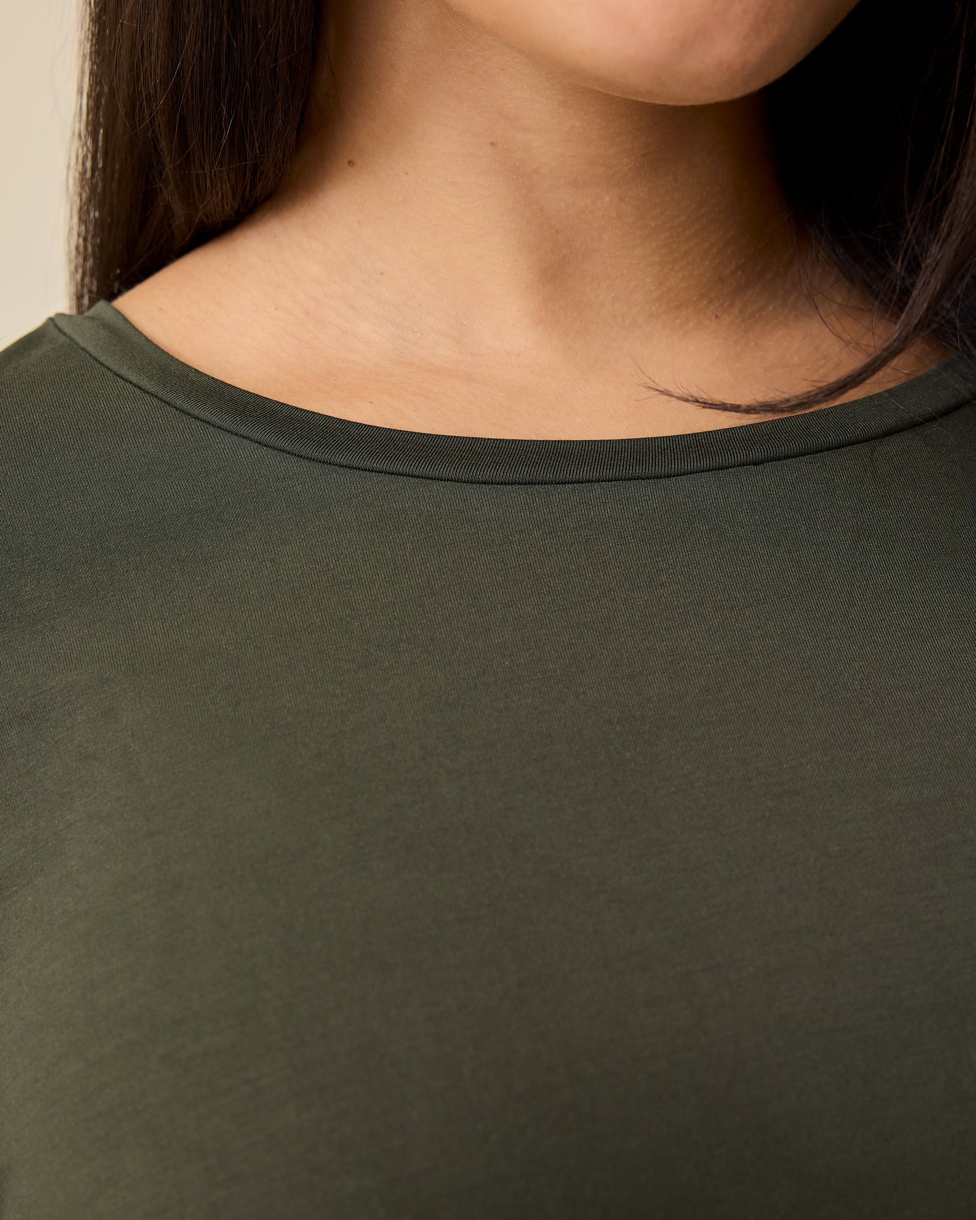 Close up of the neckline on model wearing Aria Bamboo Casual Cropped Long Sleeve Top in Thyme on a beige background.