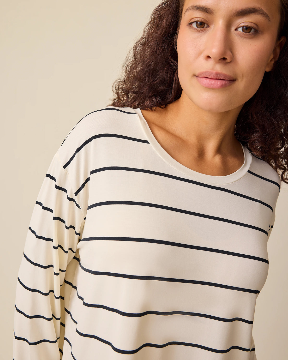 Close up of model wearing Aria Bamboo Casual Cropped Long Sleeve Top in White & Black Stripe on a beige background.