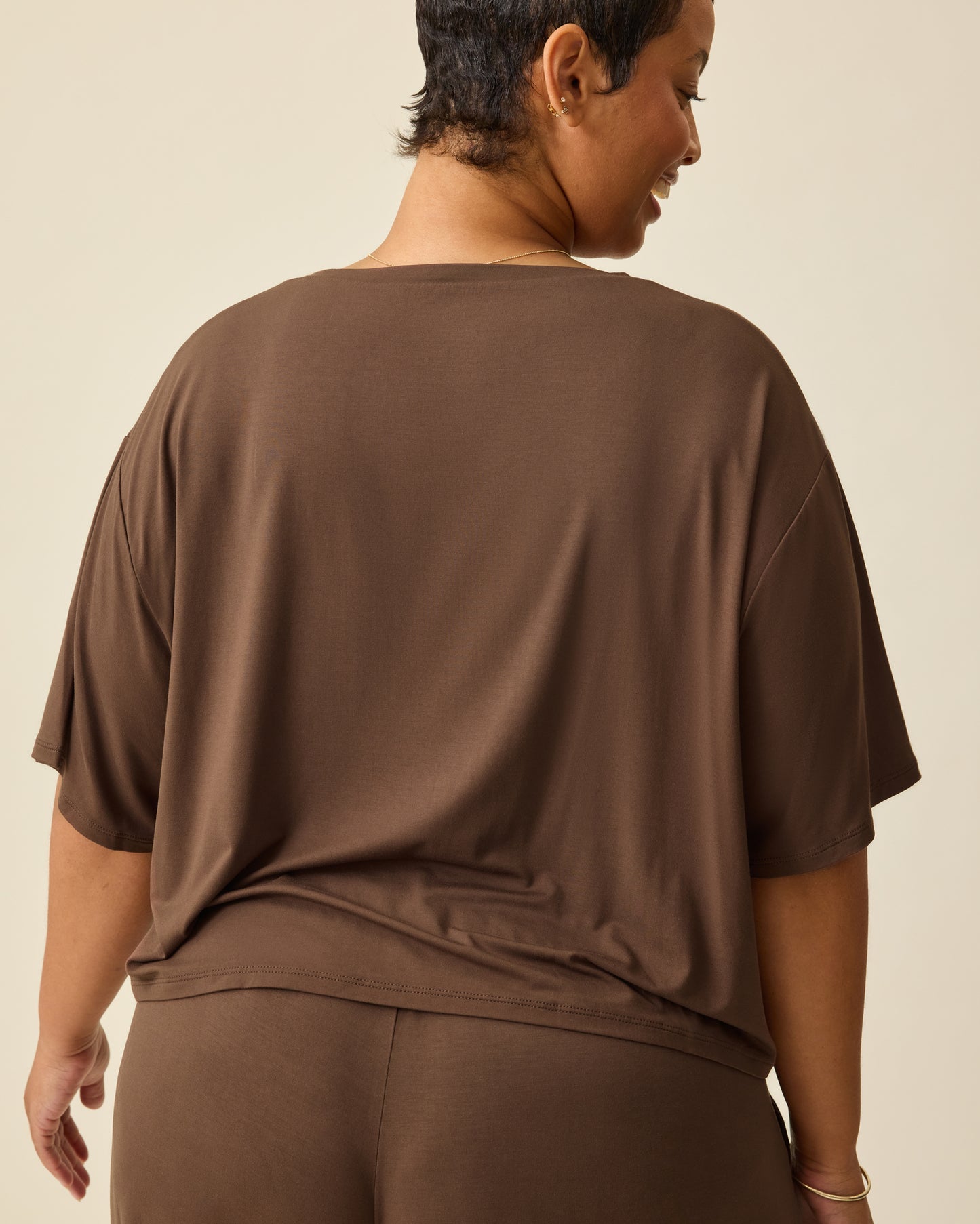 Back view of model wearing Aria Bamboo Casual Cropped Short Sleeve Top in Chocolate and Aria Bamboo Casual Lounge Pant in Chocolate, on a beige background. 