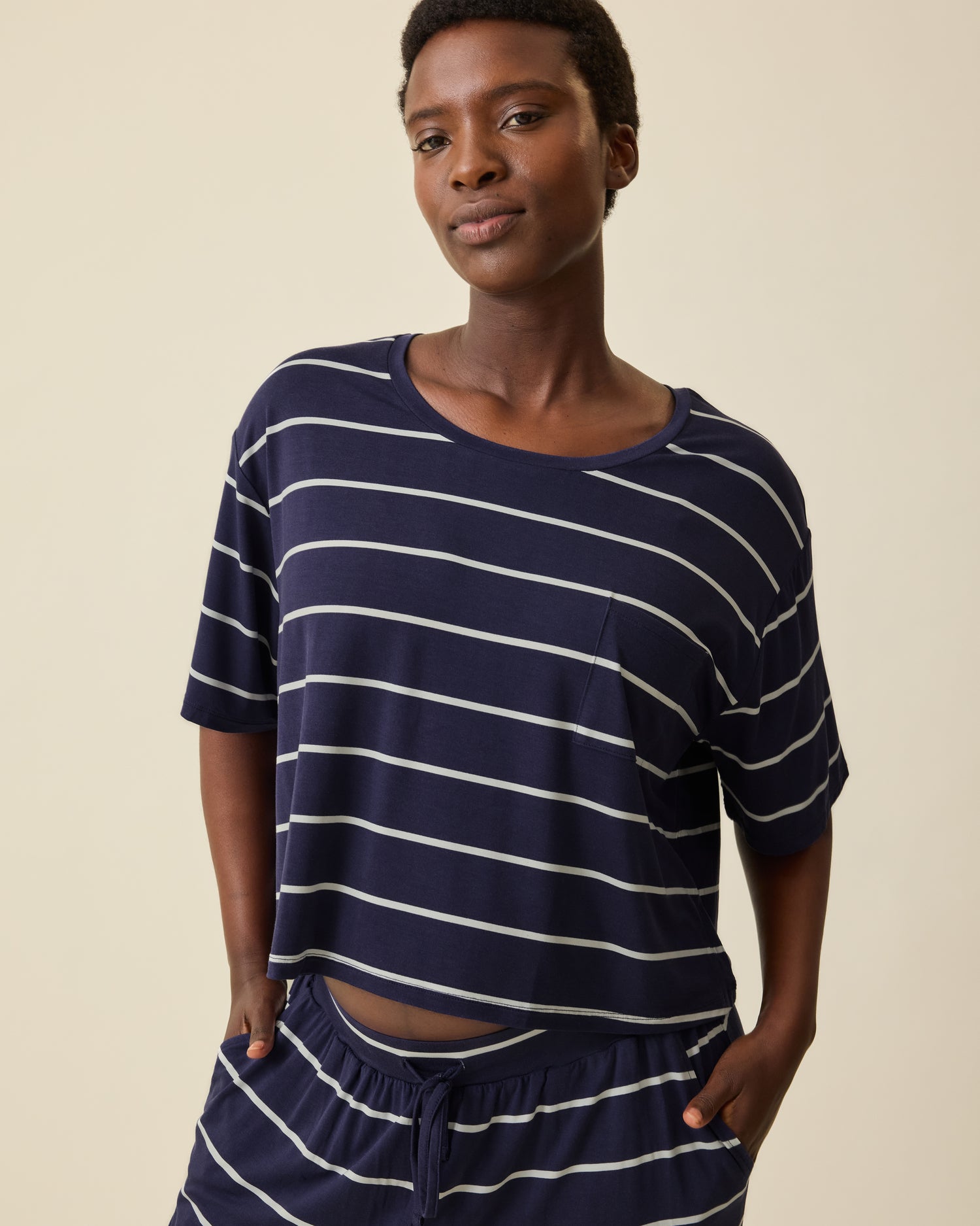 Model is wearing Aria Bamboo Casual Cropped Short Sleeve Top in Navy & White Stripe and Aria Bamboo Casual Lounge Pant in Navy & White Stripe on a beige background. @model_info:Anna is wearing a Small.
