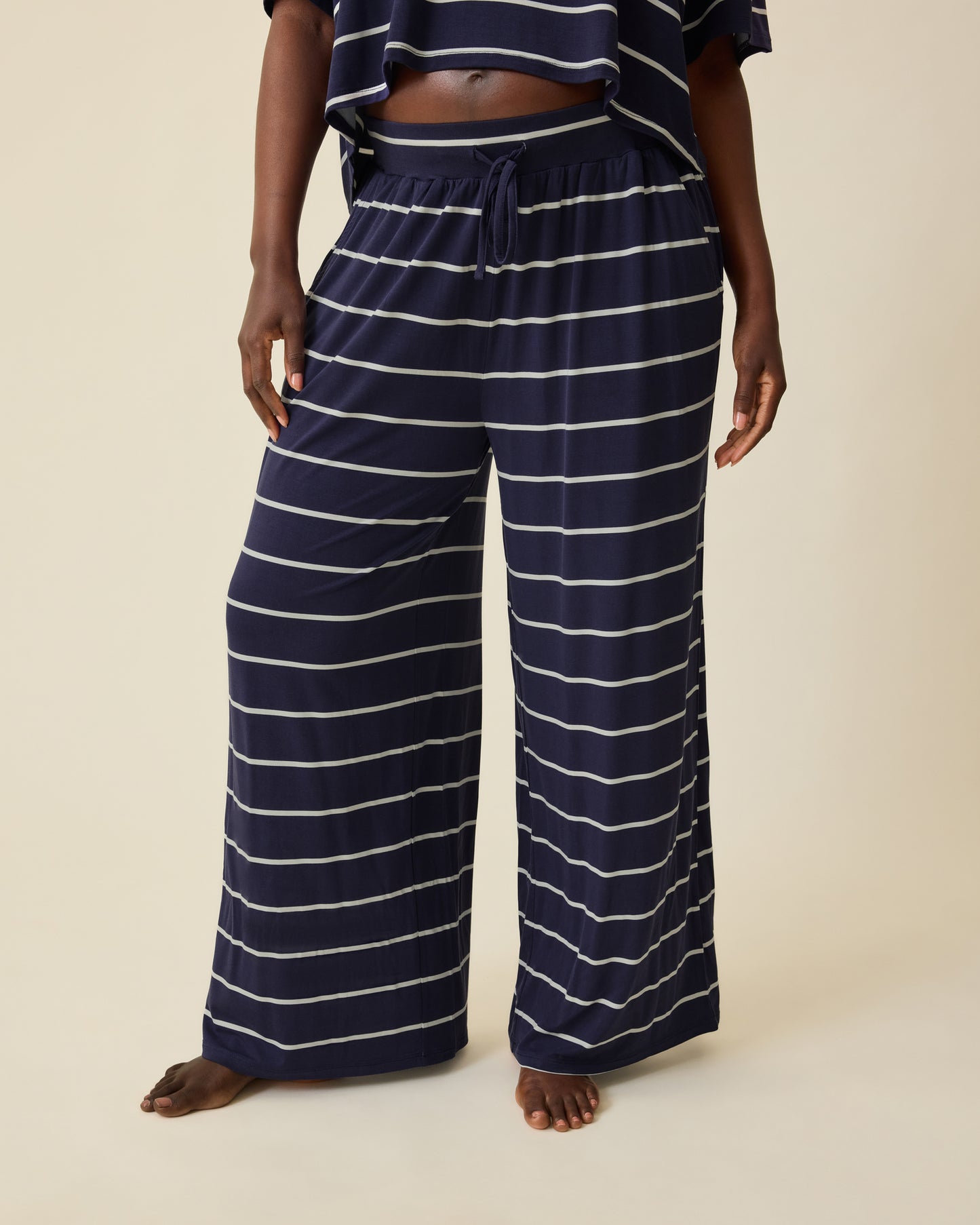 Model is wearing Aria Bamboo Casual Cropped Short Sleeve Top in Navy & White Stripe and Aria Bamboo Casual Lounge Pant in Navy & White Stripe on a beige background. @model_info:Anna is 5'8.5" and wearing a Medium.