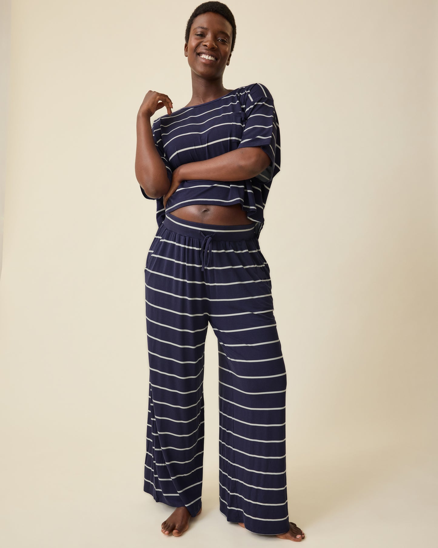 Model is wearing Aria Bamboo Casual Cropped Short Sleeve Top in Navy & White Stripe and Aria Bamboo Casual Lounge Pant in Navy & White Stripe on a beige background.