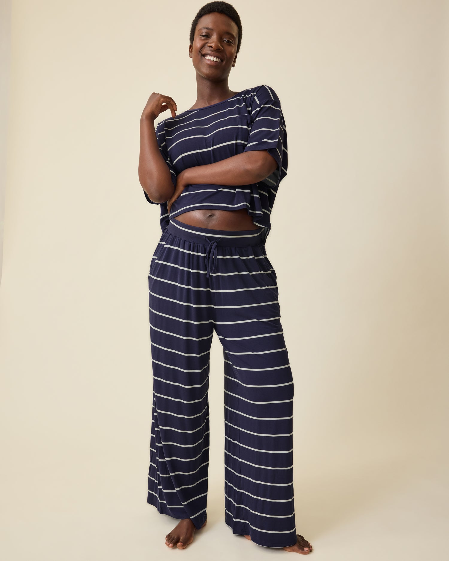 Model is wearing Aria Bamboo Casual Cropped Short Sleeve Top in Navy & White Stripe and Aria Bamboo Casual Lounge Pant in Navy & White Stripe on a beige background.