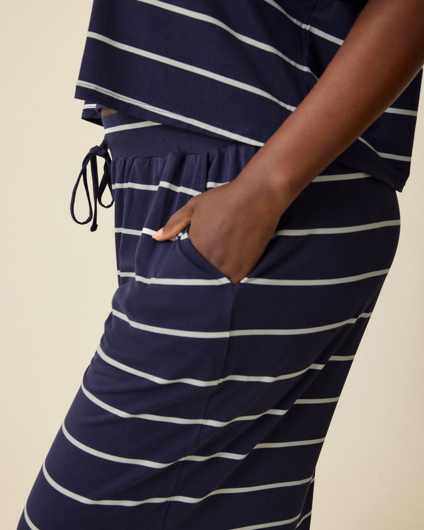 Side view of Model wearing Aria Bamboo Casual Cropped Short Sleeve Top in Navy & White Stripe and Aria Bamboo Casual Lounge Pant in Navy & White Stripe on a beige background.