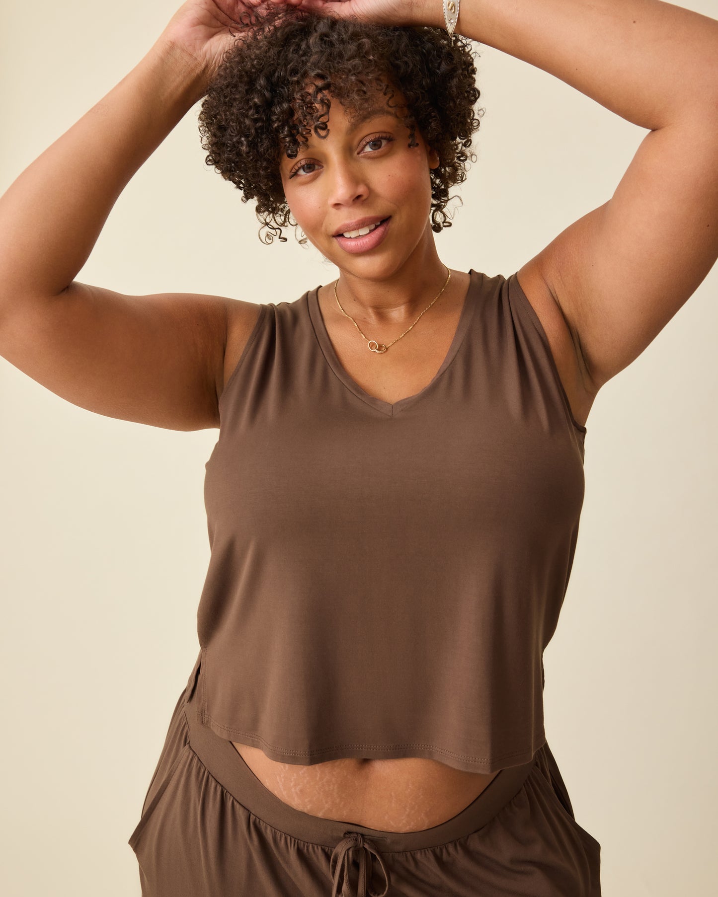 Model is wearing Aria Bamboo Cropped V-neck Tank in Chocolate and Aria Bamboo Casual Lounge Pant in Chocolate on a beige backgound. @model_info:Skye is wearing a Large.