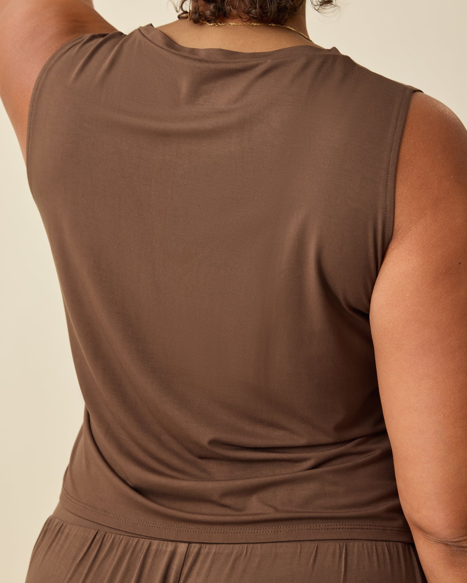 Back view of the Aria Bamboo Cropped V-neck Tank in Chocolate on a beige backgound.