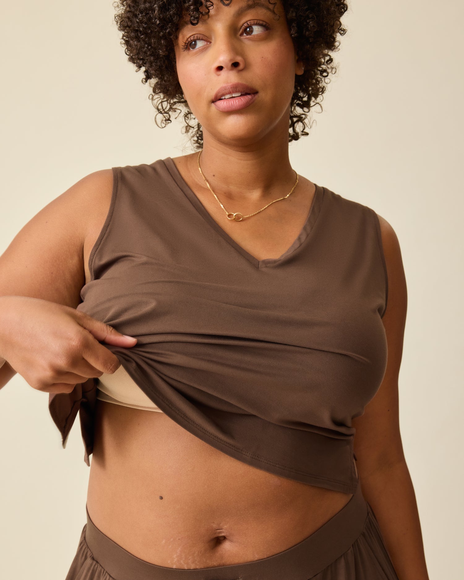 Model is wearing Aria Bamboo Cropped V-neck Tank in Chocolate, displaying the easy nursing access, and Aria Bamboo Casual Lounge Pant in Chocolate on a beige backgound.