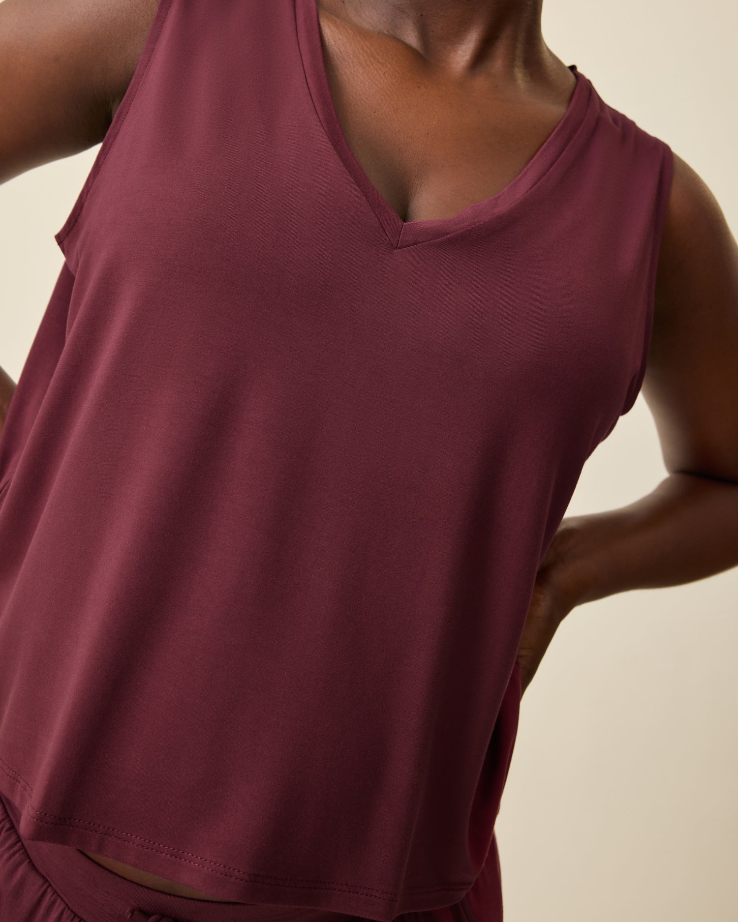 Close up of wearing Aria Bamboo Cropped V-neck Tank in Deep Burgundy and Aria Bamboo Casual Lounge Pant in Deep Burgundy on a beige background.