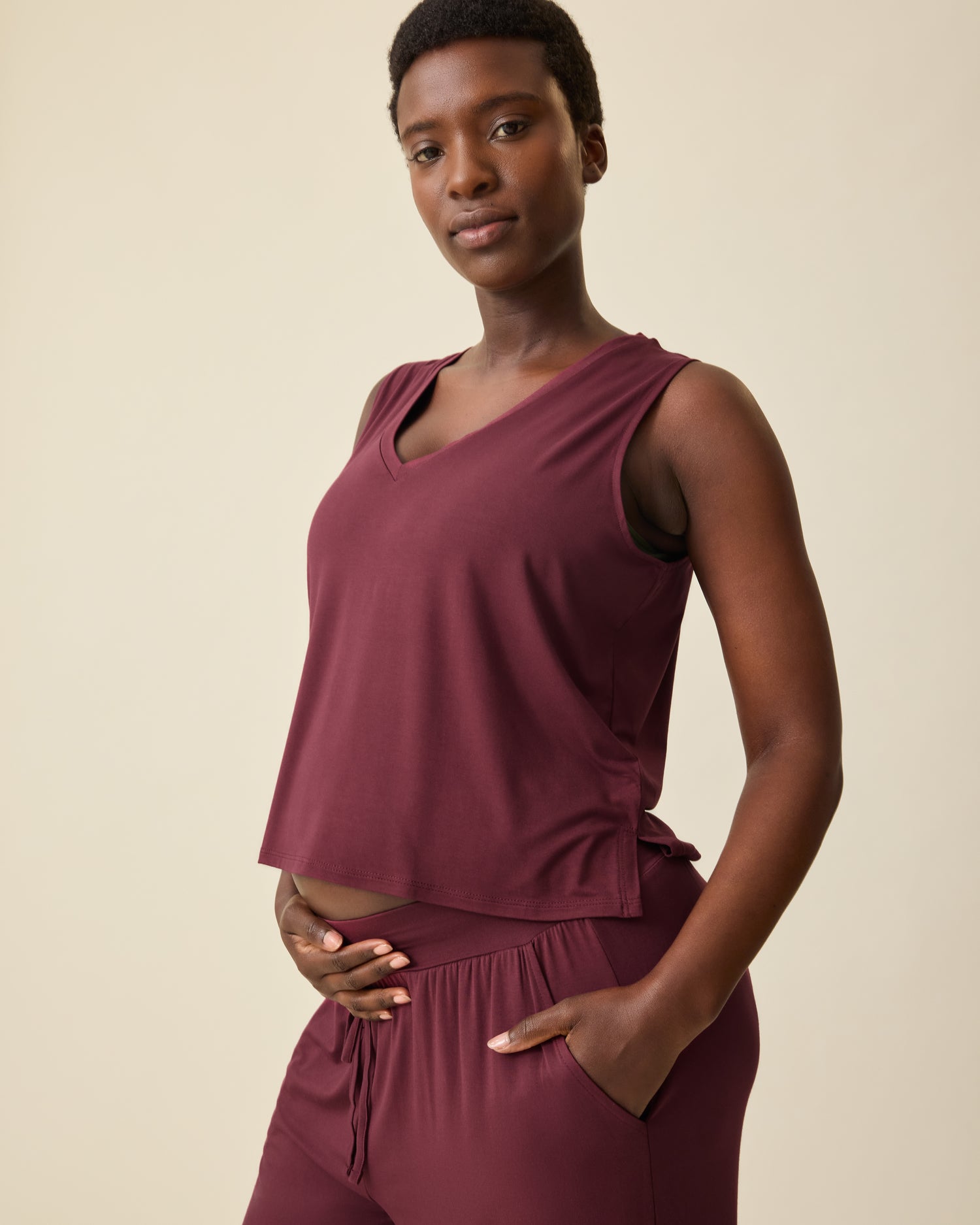 Close up of wearing Aria Bamboo Cropped V-neck Tank in Deep Burgundy and Aria Bamboo Casual Lounge Pant in Deep Burgundy on a beige background. @model_info:Anna is wearing a Small.