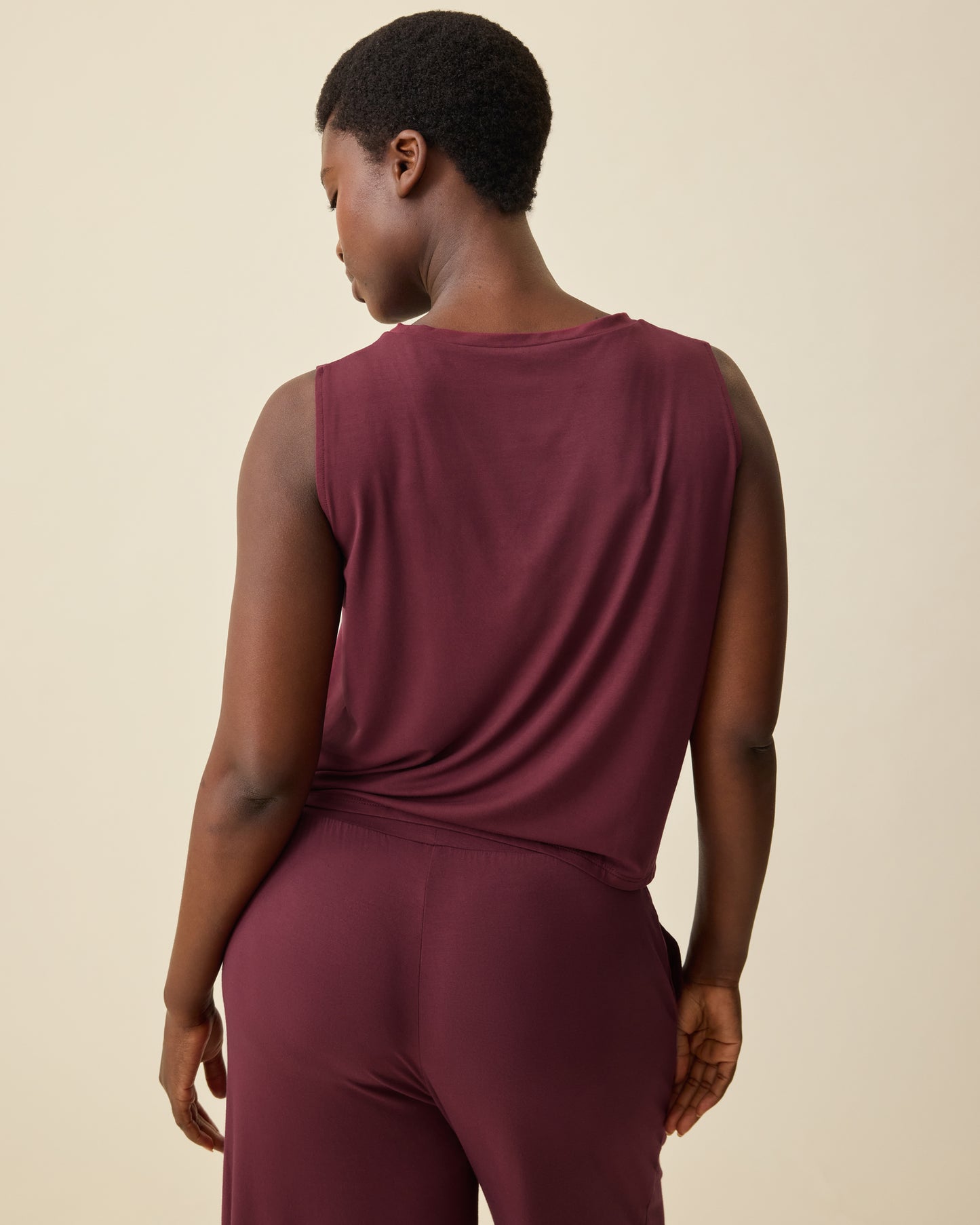 Back view of Aria Bamboo Cropped V-neck Tank in Deep Burgundy and Aria Bamboo Casual Lounge Pant in Deep Burgundy on a beige background.