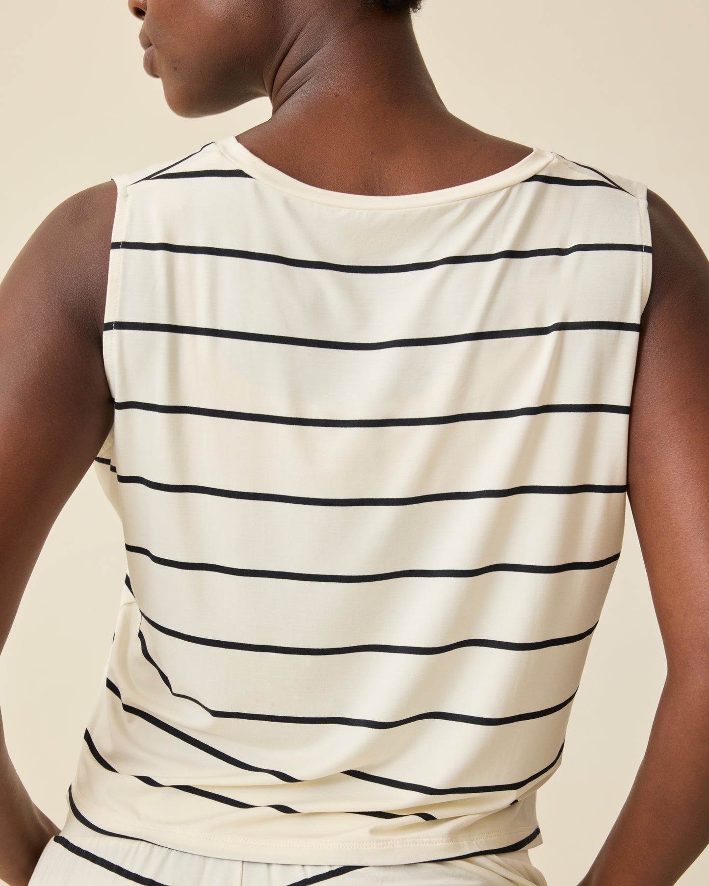 Back view of Aria Bamboo Cropped V-neck Tank in White & Black Stripe on a beige background.
