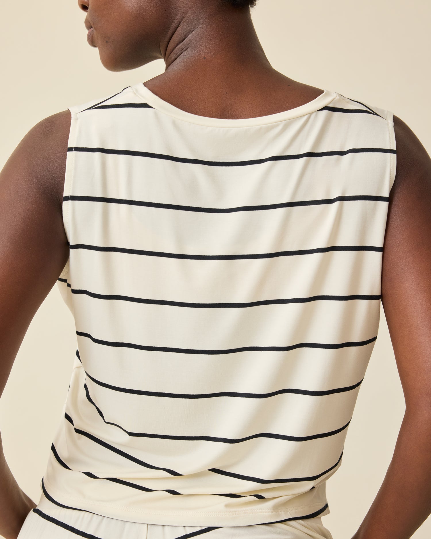 Back view of Aria Bamboo Cropped V-neck Tank in White & Black Stripe on a beige background.