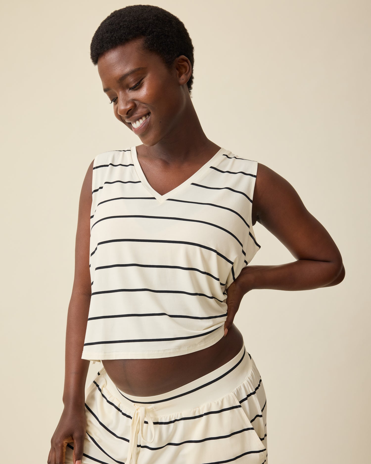 Model is wearing Aria Bamboo Cropped V-neck Tank in White & Black Stripe and Aria Bamboo Casual Lounge Short in White & Black Stripe on a beige background. @model_info:Anna is wearing a Small.