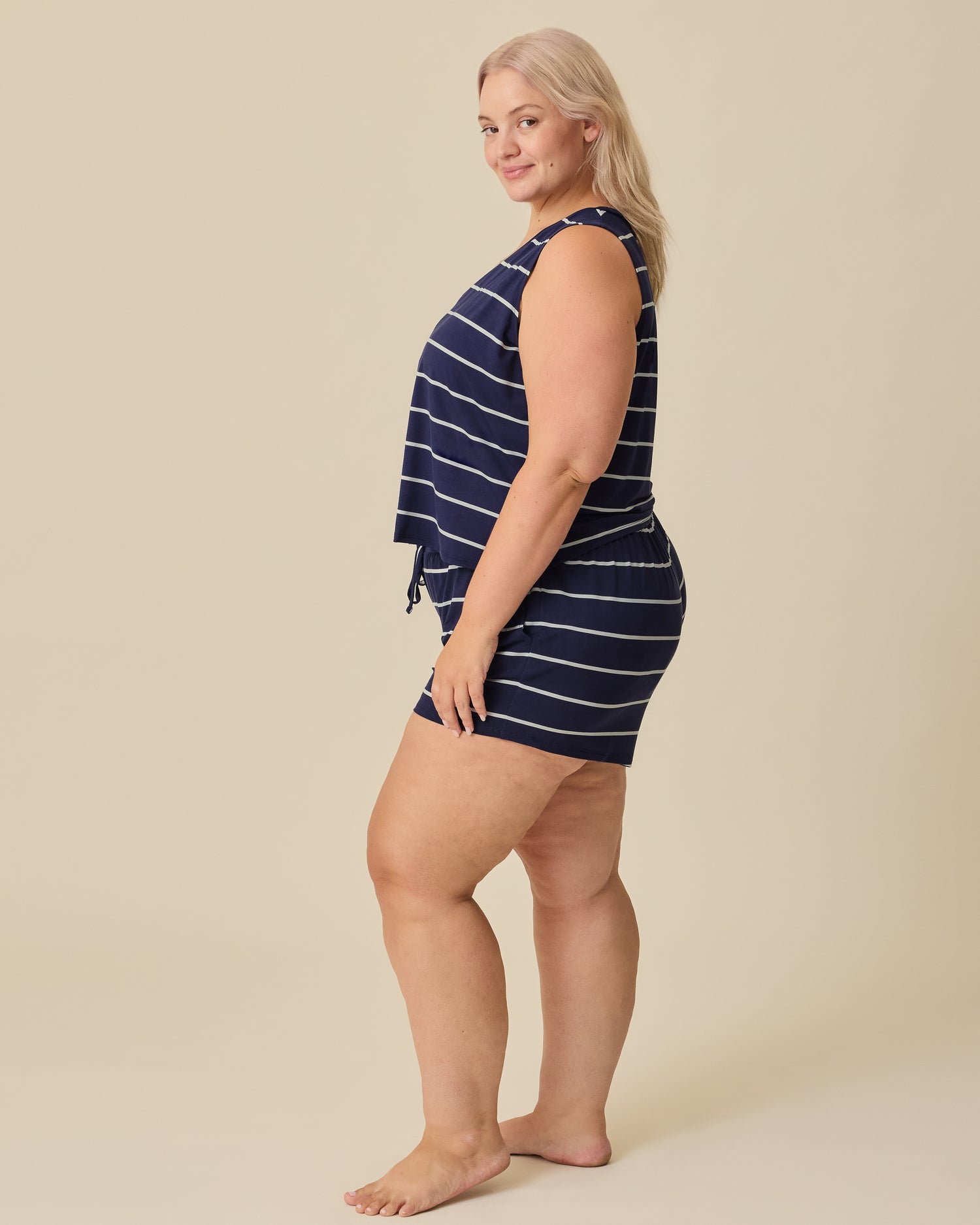 Side view of model wearing Aria Bamboo Cropped V-neck Tank and Aria Bamboo Casual Lounge Short in Navy & White Stripe on a beige background.