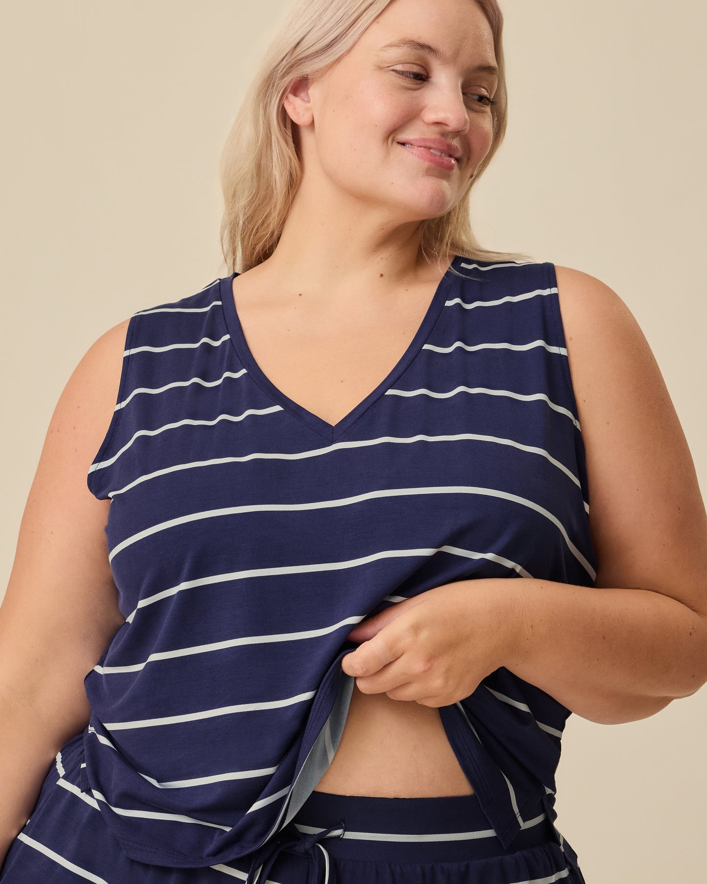 Model showing easy breastfeeding access on the Aria Bamboo Cropped V-neck Tank in Navy & White Stripe on a beige background.