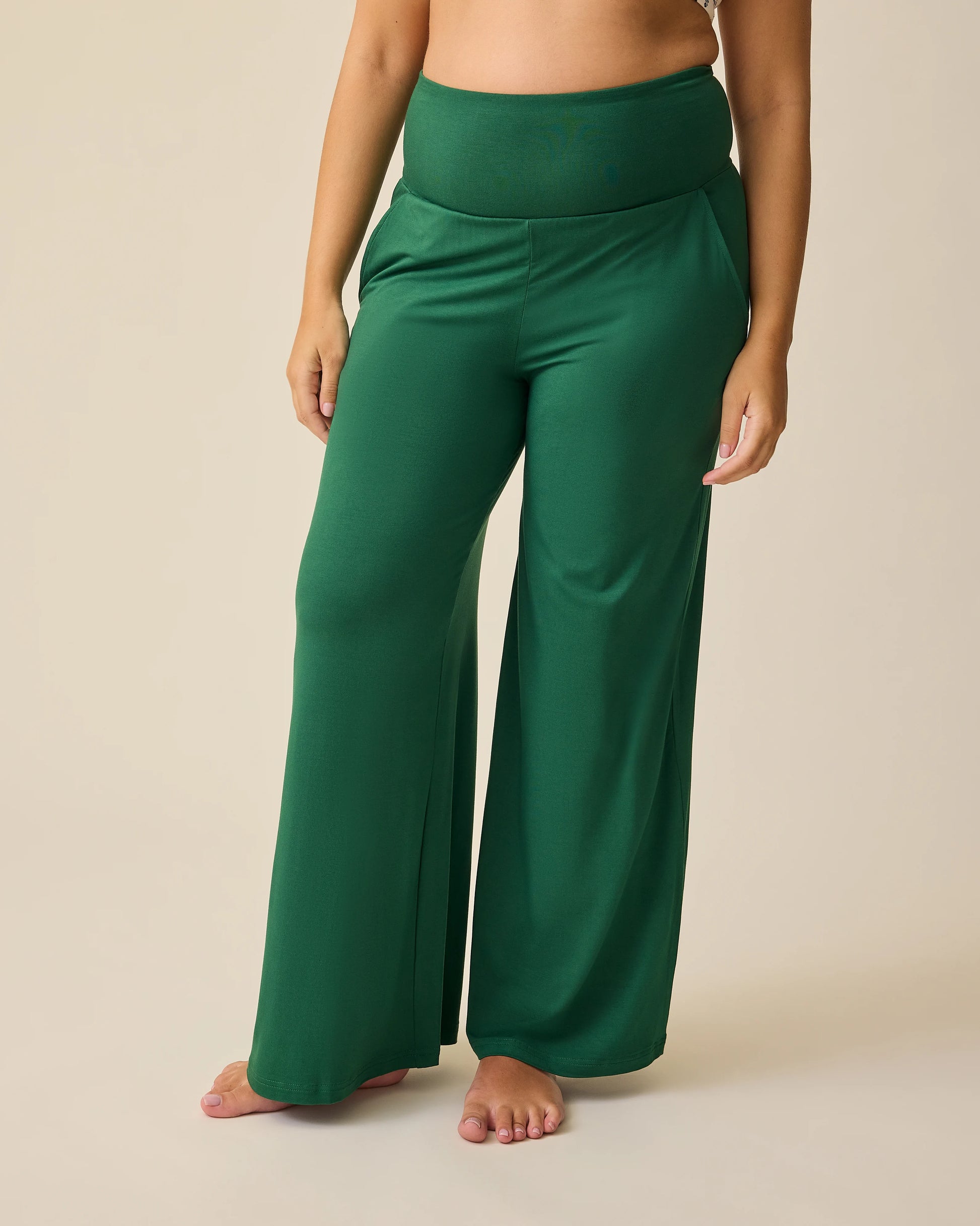 Model is wearing Bamboo Wide Leg Maternity & Postpartum Lounge Pant in Deep Green on a beige background. @model_info:Brianna is 5'8" and wearing a Small.