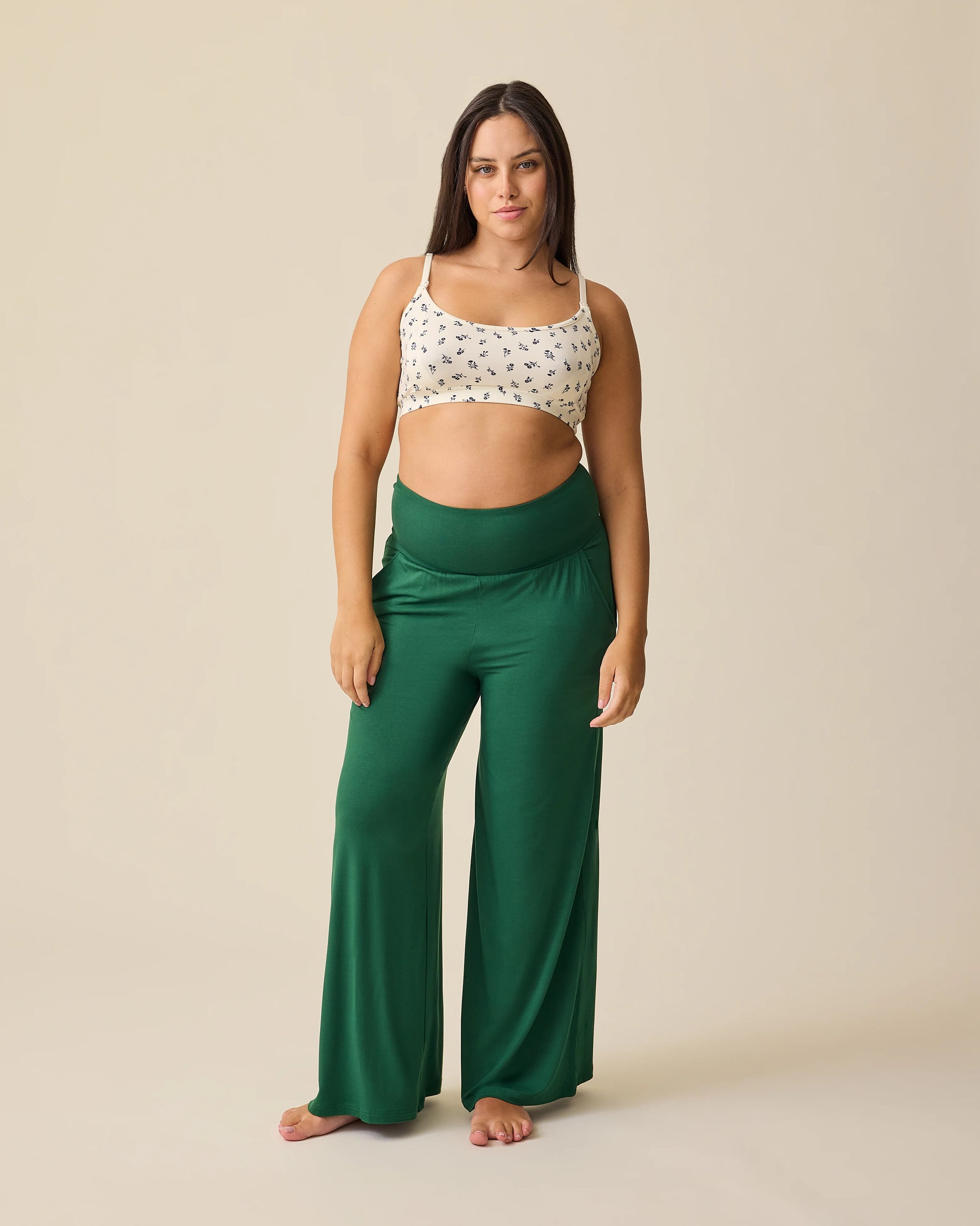Model is wearing Bamboo Wide Leg Maternity & Postpartum Lounge Pant in Deep Green on a beige background. 